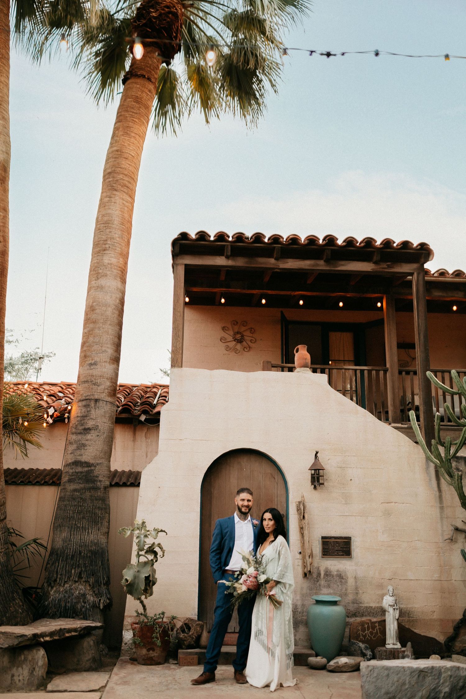 Desert wedding venue with Spanish architecture, palm trees, and string lights at sunset.