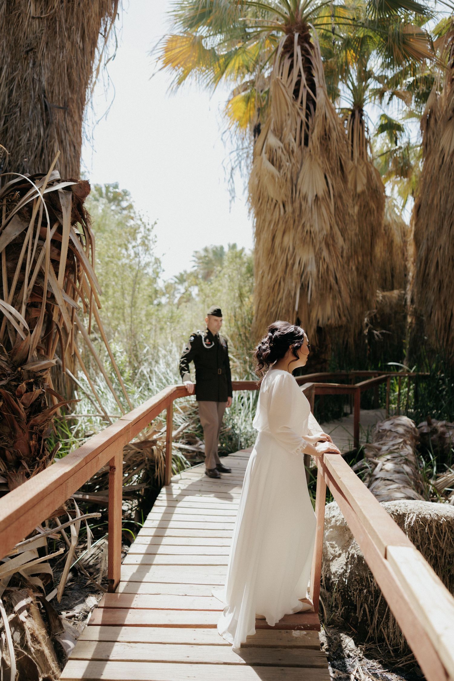 A sequence of photos showing a wedding couple walking along a wooden boardwalk surrounded by palm trees in a desert oasis.