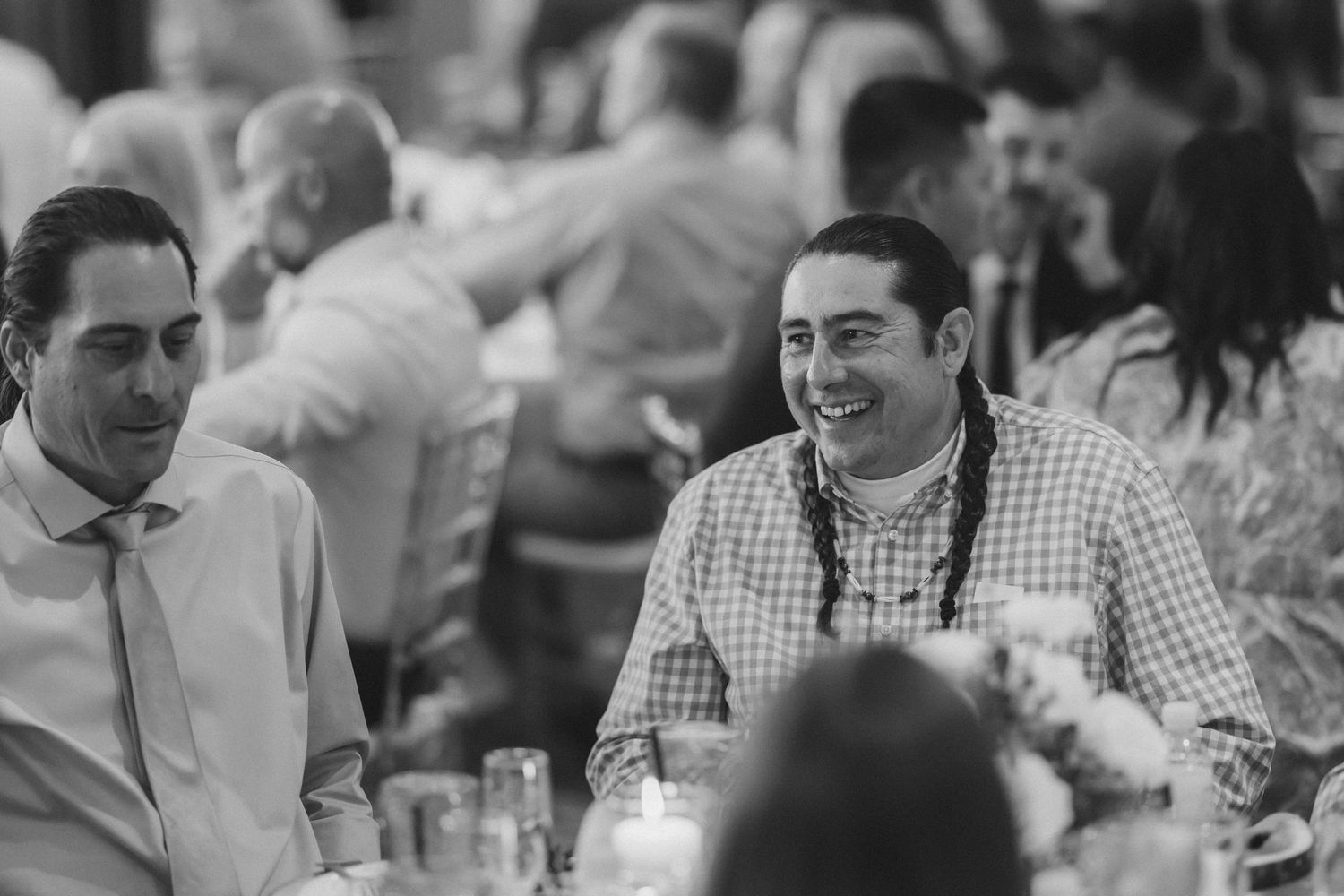 Black and white photo of wedding guests laughing and enjoying conversation at a reception dinner table.