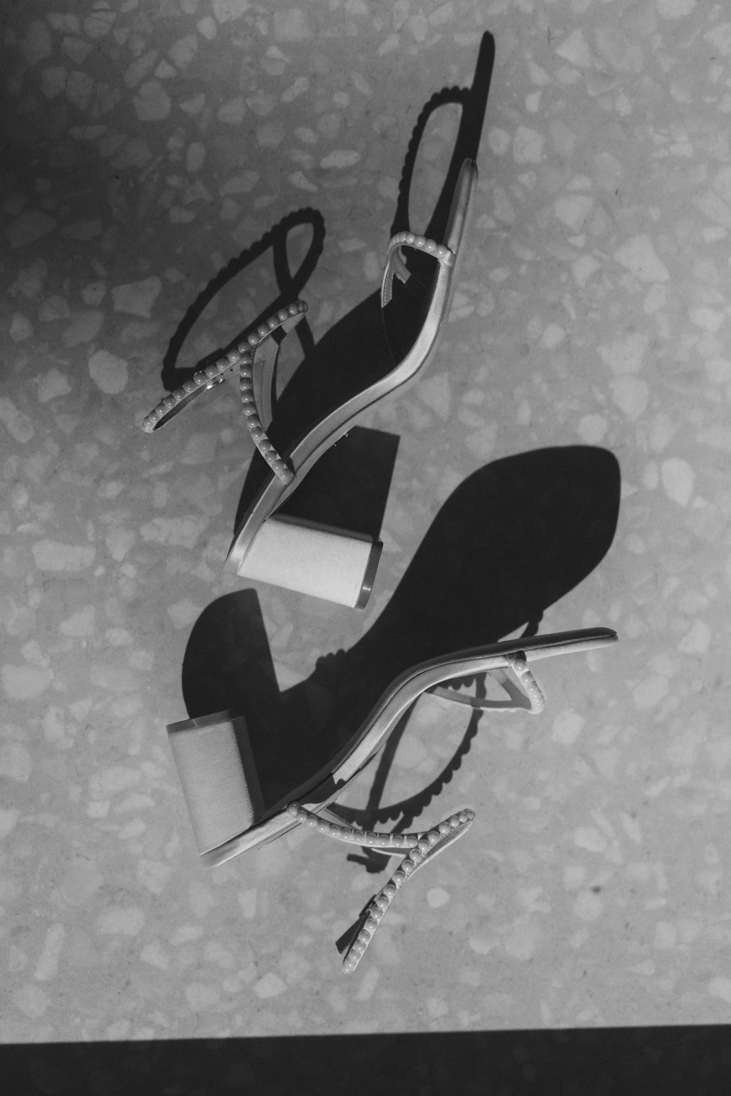 Black and white photo of bridal heels with crystal embellishments on terrazzo floor.