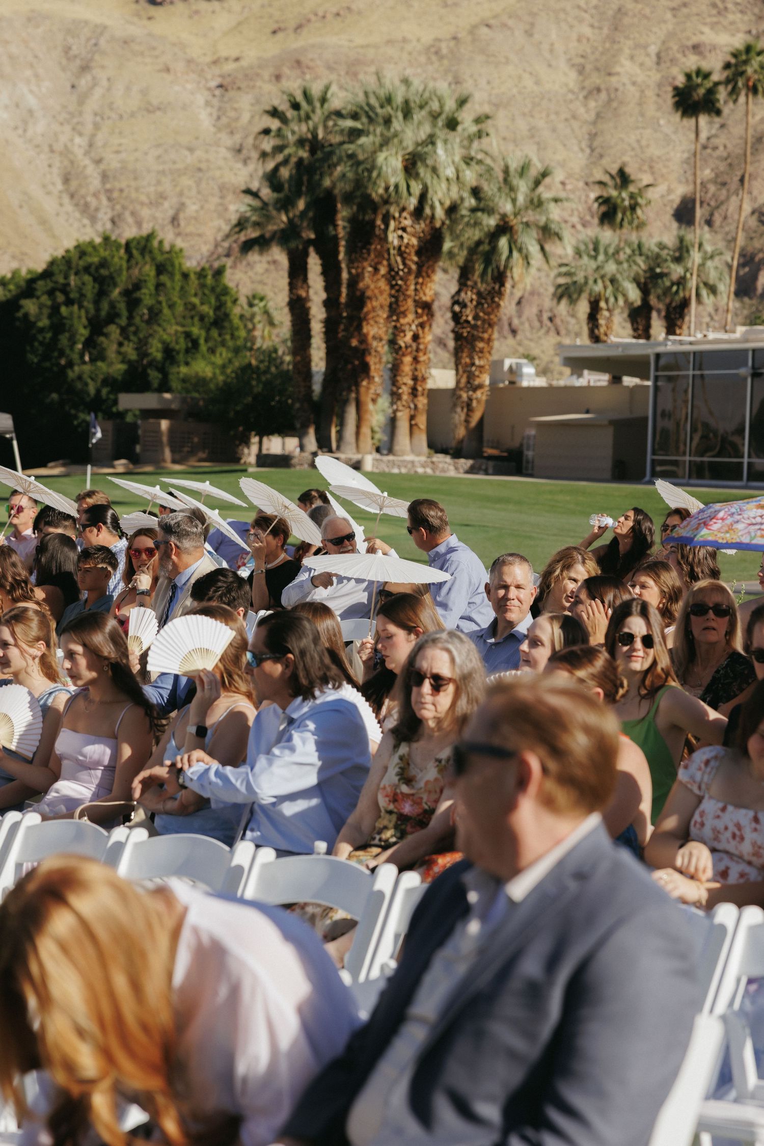 Wedding ceremony guests seated outdoors in Palm Springs with parasols and mountain backdrop.