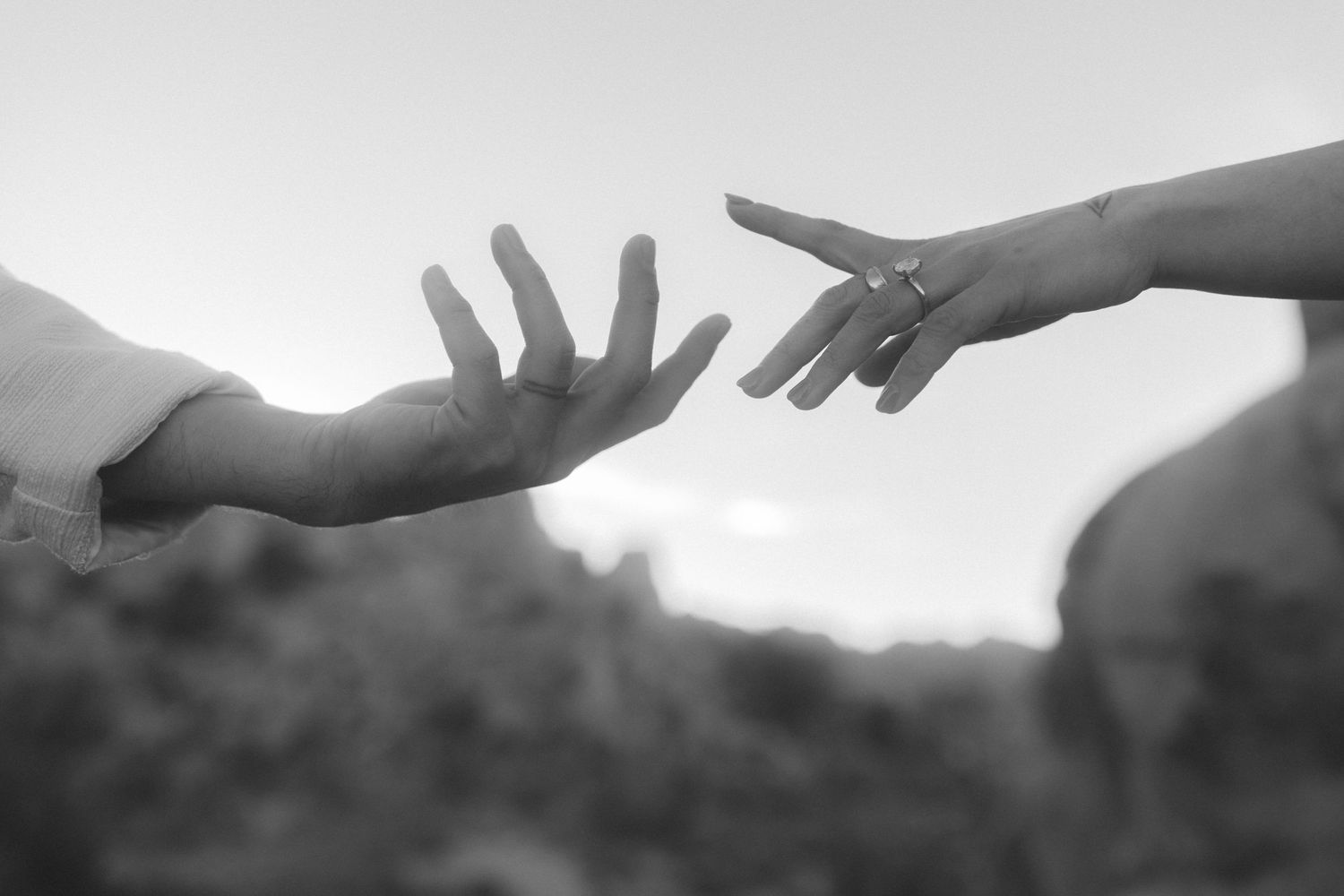 Two hands reaching toward each other in black and white, symbolizing connection and love, with a ring visible on one finger.