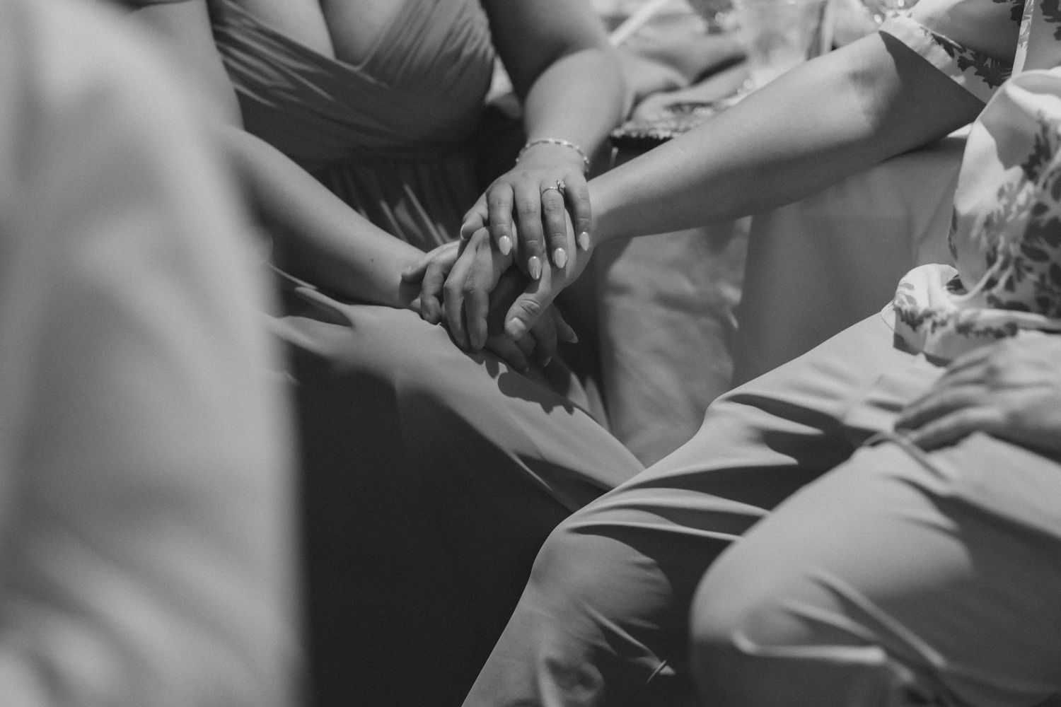 Close-up black and white photo of wedding guests holding hands together in support during emotional ceremony moment.