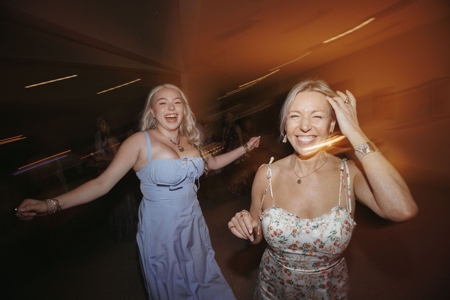 Two women laughing and dancing joyfully together on the dance floor at a wedding reception.