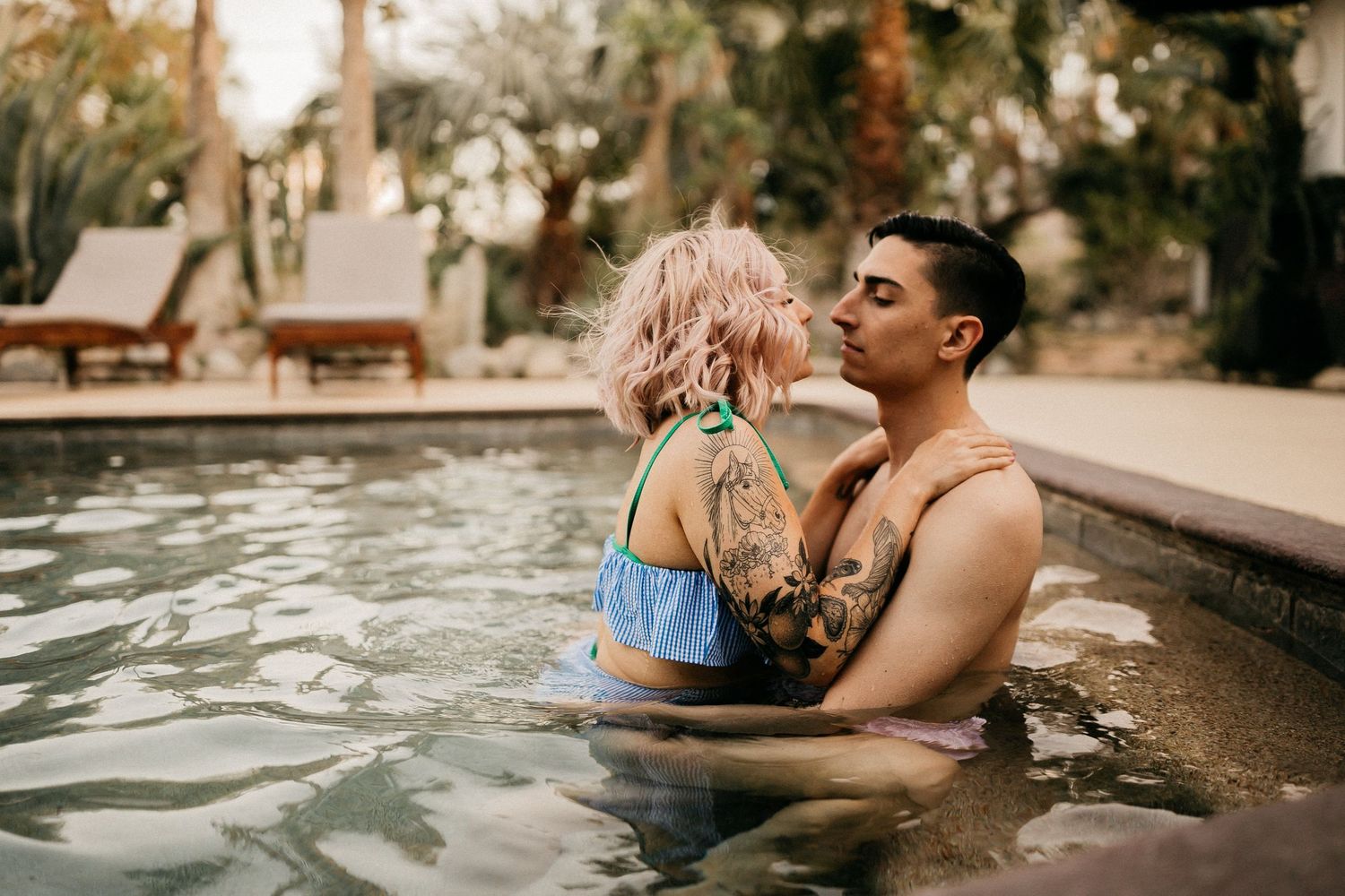 Couple sharing romantic moments together in natural swimming pool beneath orange sunset light.