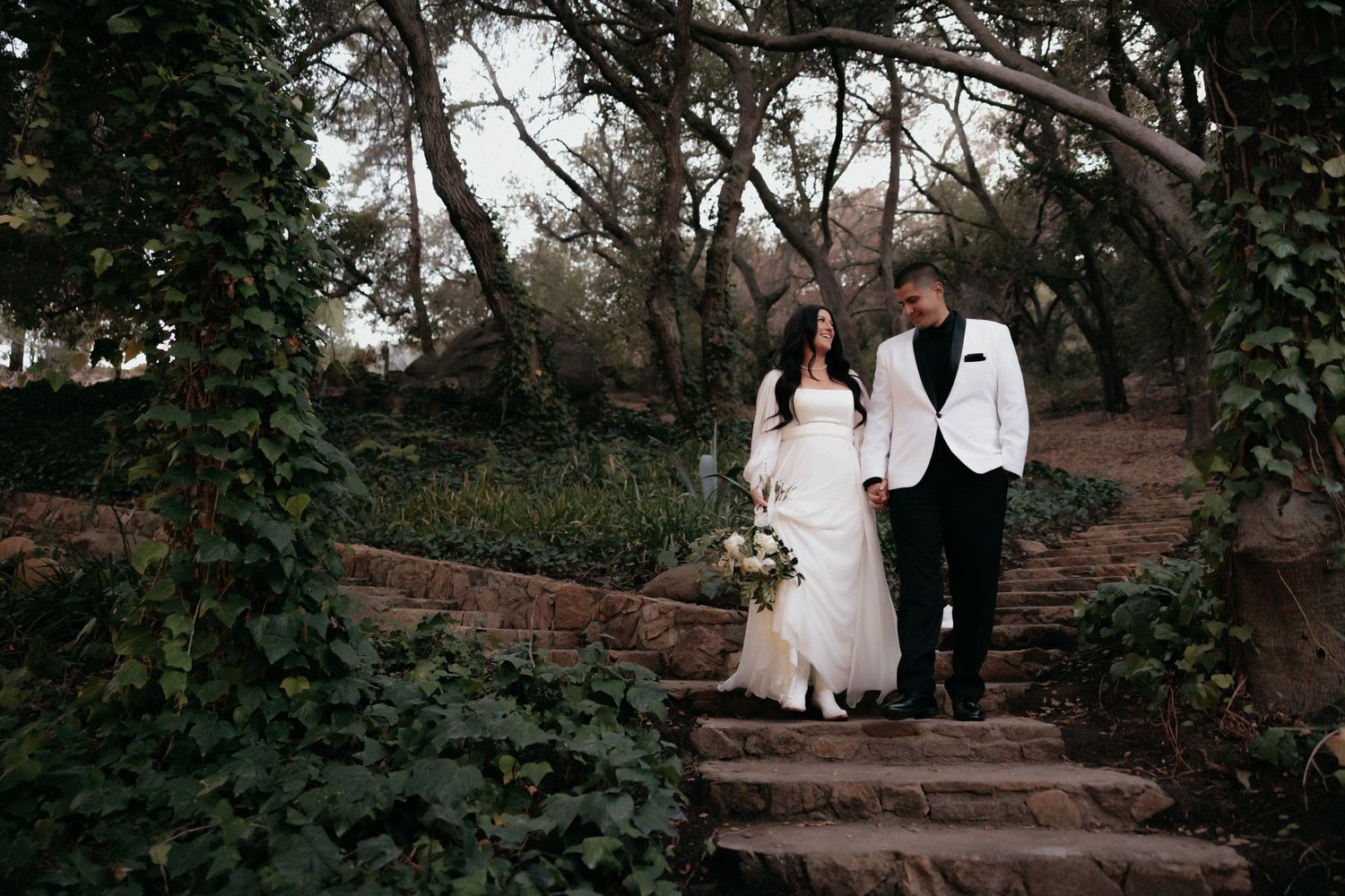 Couple walking up rustic stone garden steps surrounded by lush foliage during an outdoor photo session.
