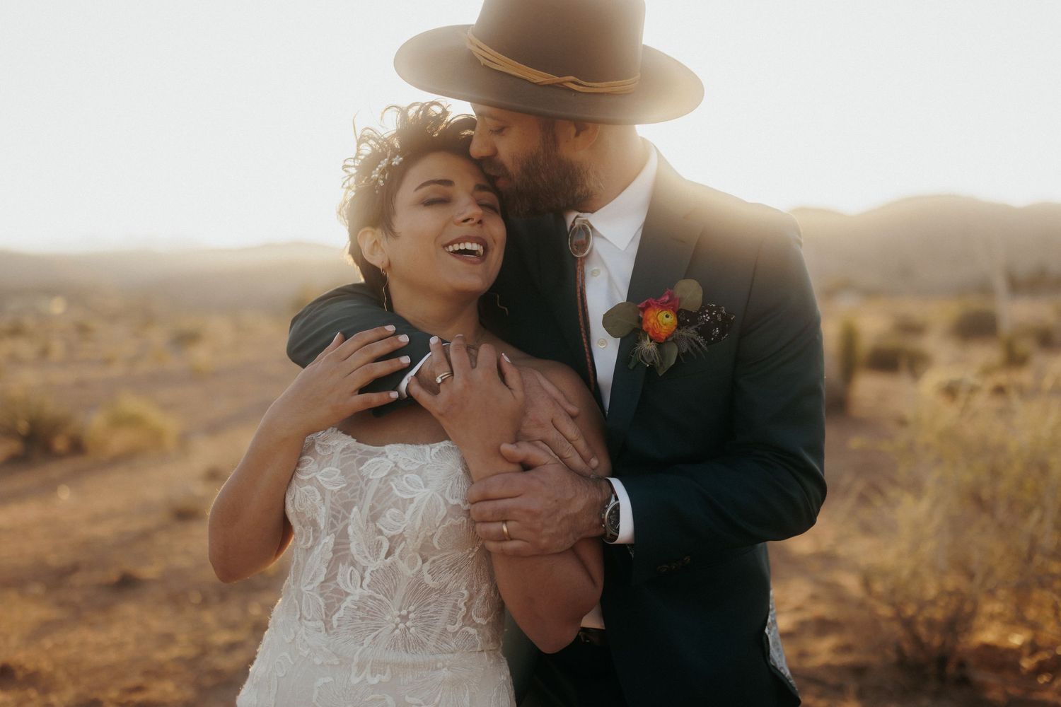 Couple embraces during golden hour photoshoot in rustic desert landscape wearing formal wedding attire.