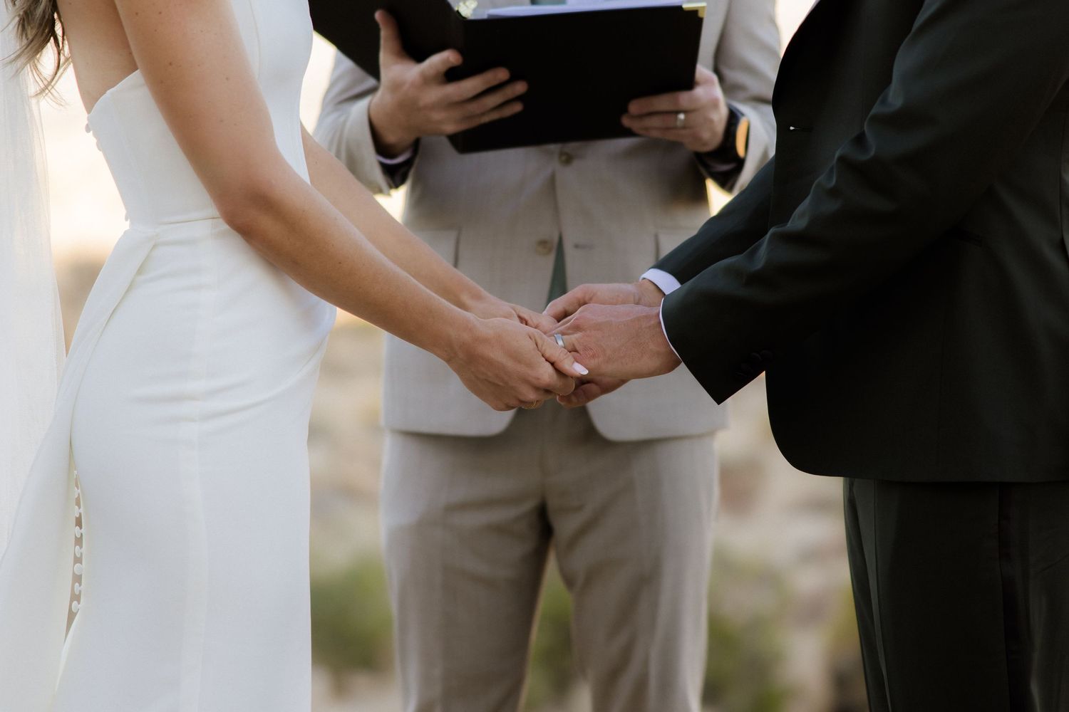 Close-up shot of hands exchanging wedding rings during an outdoor ceremony.