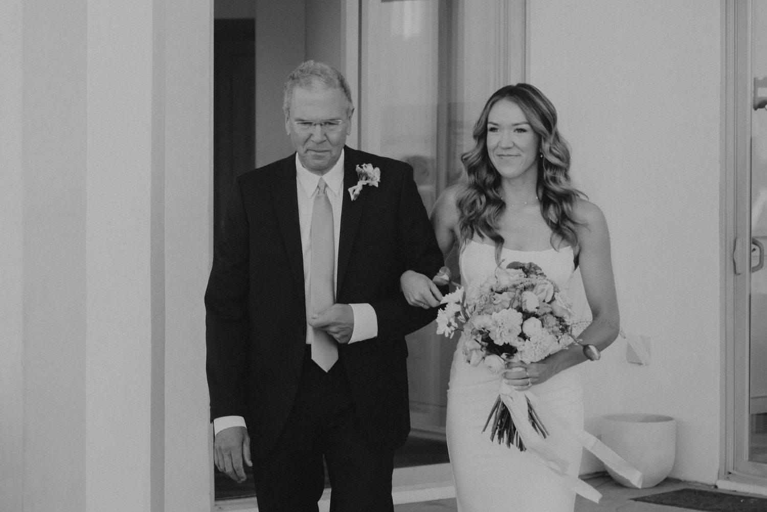A black and white wedding photo shows a happy couple walking down the hallway of an elegant venue.