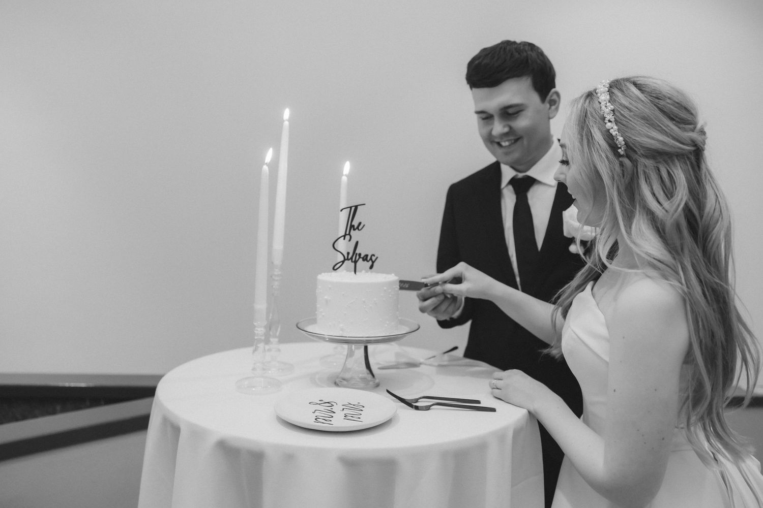 Bride and groom cutting their white wedding cake with a custom name topper in black and white.