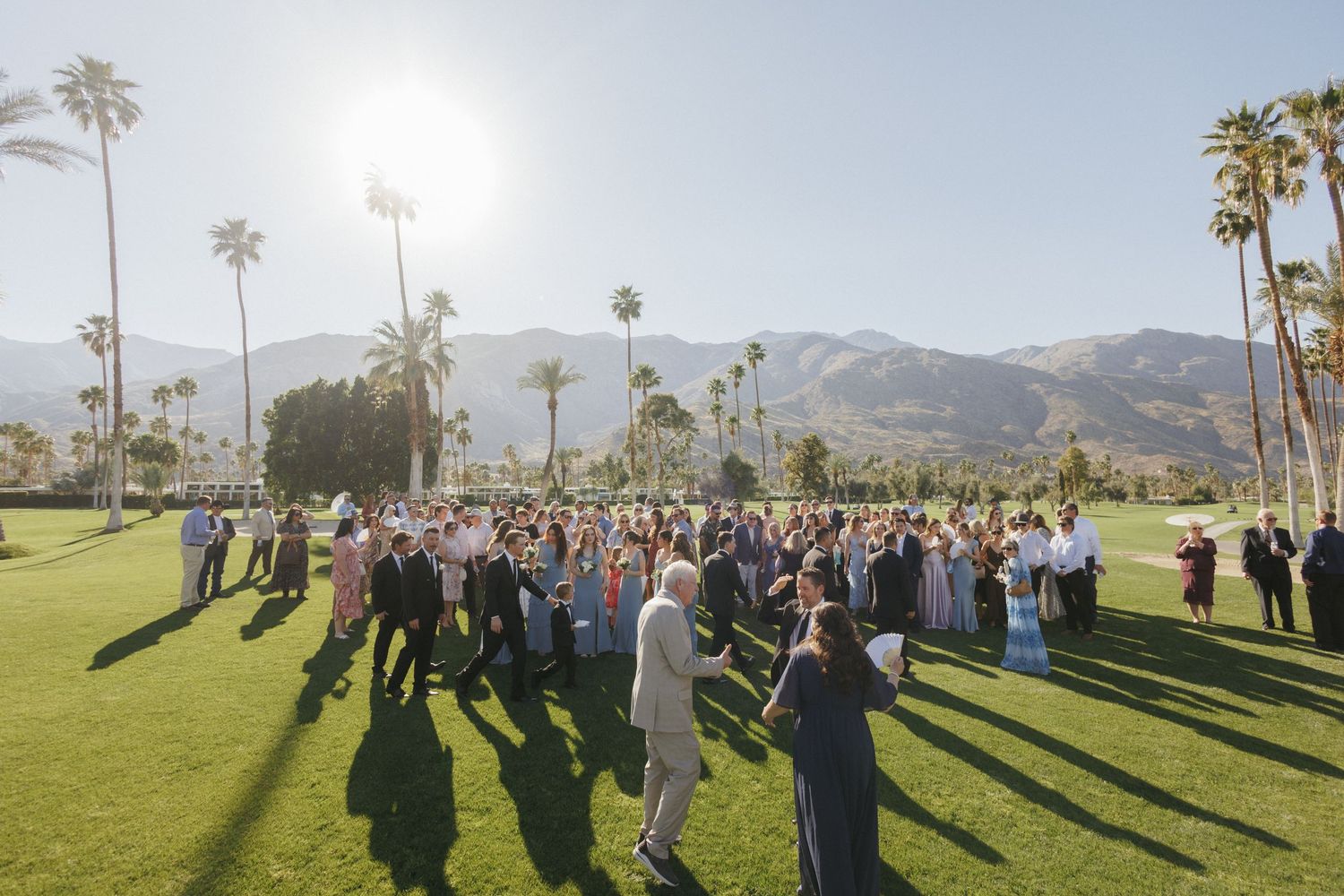 Outdoor wedding ceremony on green lawn with palm trees and mountain backdrop in Palm Springs.
