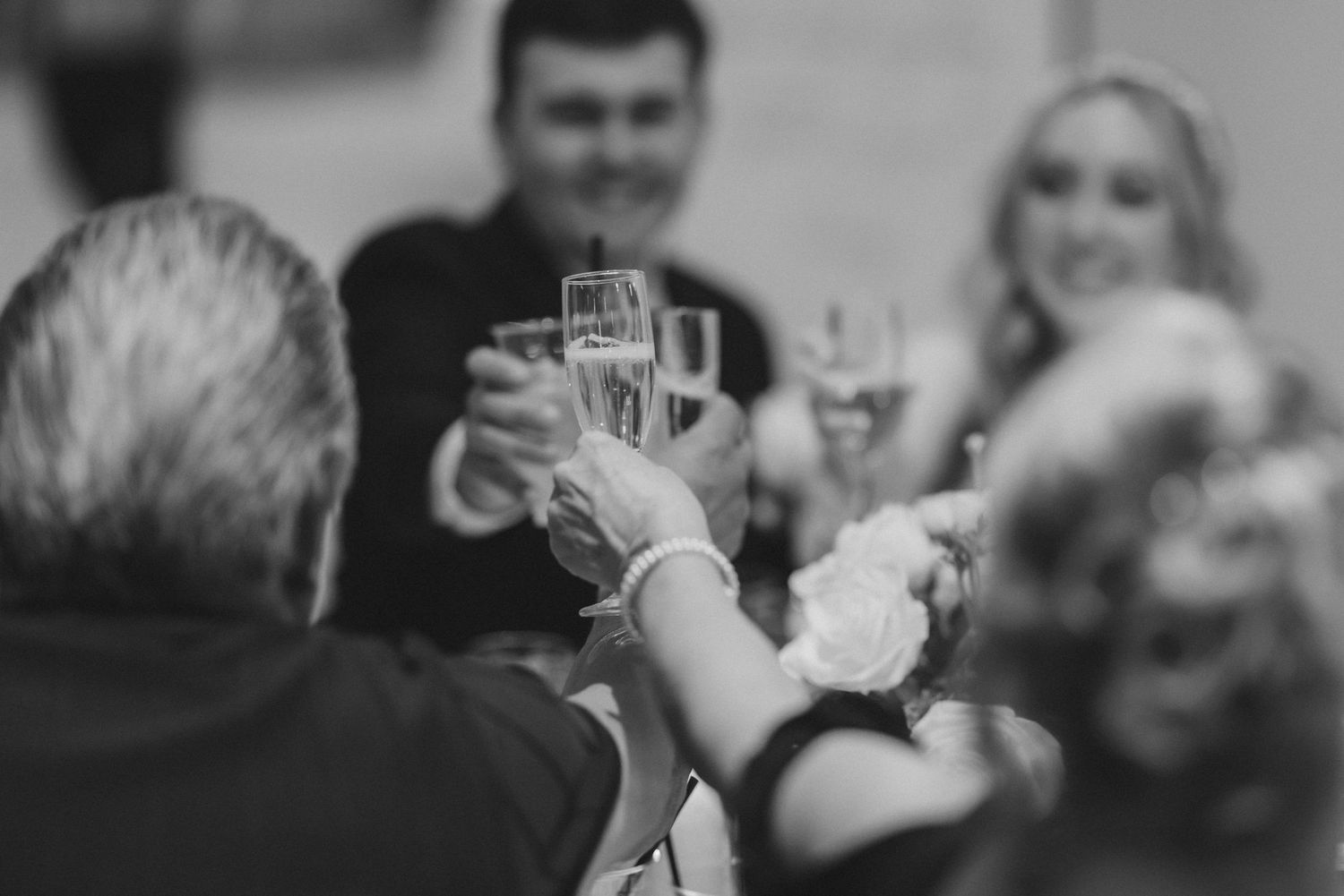 Black and white photo of wedding guests raising champagne glasses in a toast.