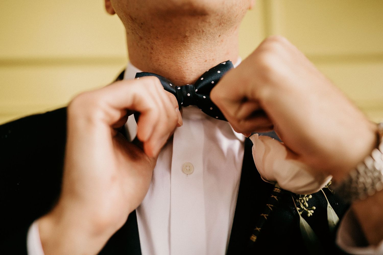 Closeup sequence showing hands adjusting a bowtie on a white formal shirt collar.