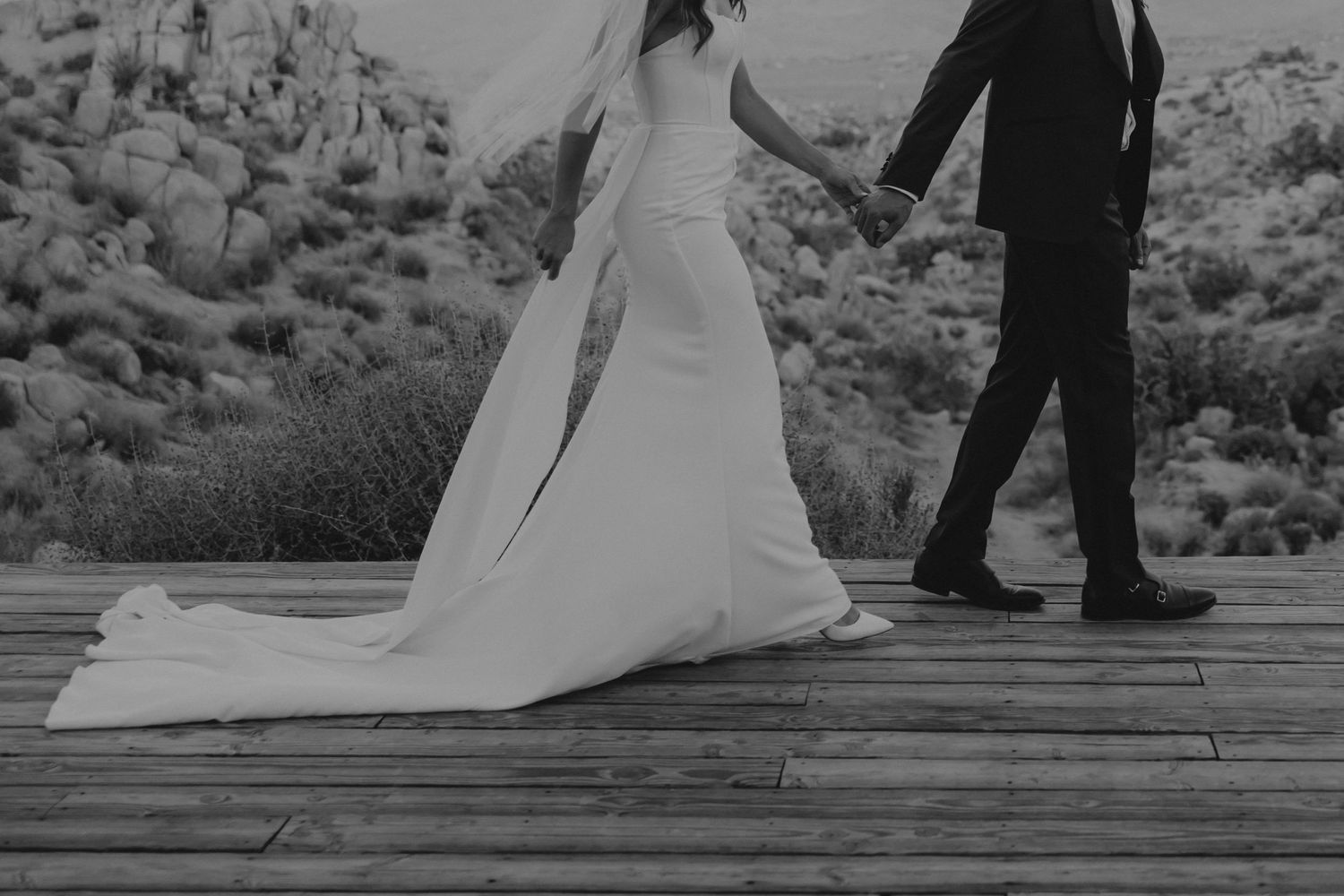Newlywed couple walking together on rustic wooden dock at sunset.
