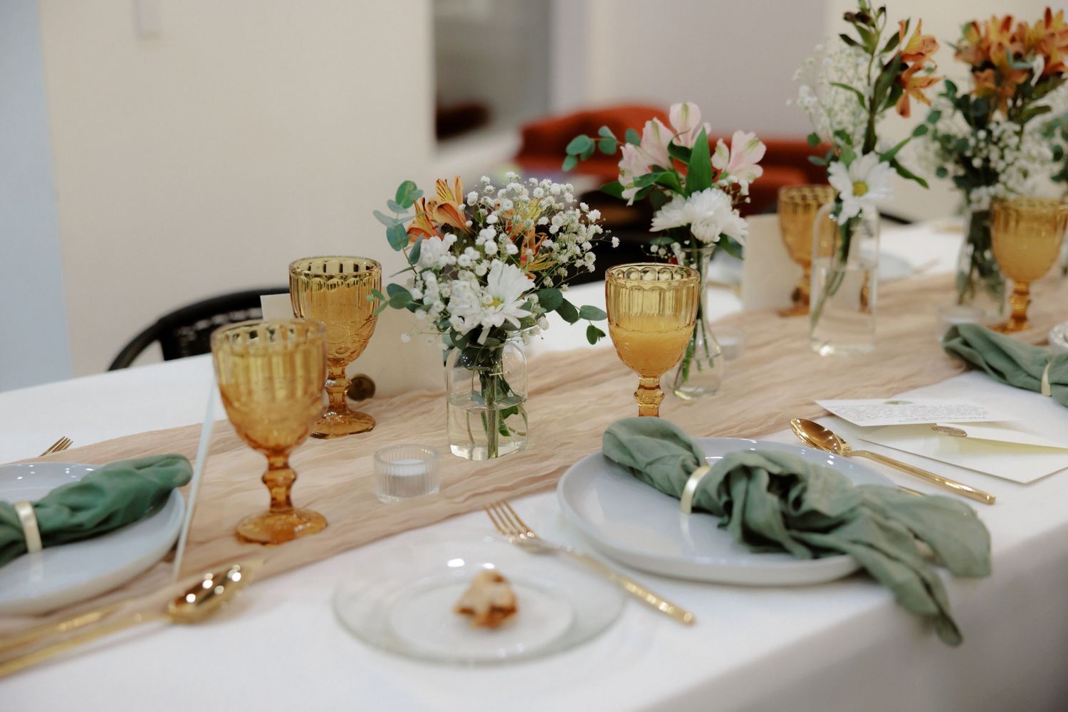Elegant wedding table settings with amber glassware, white floral centerpieces, and sage green accents.