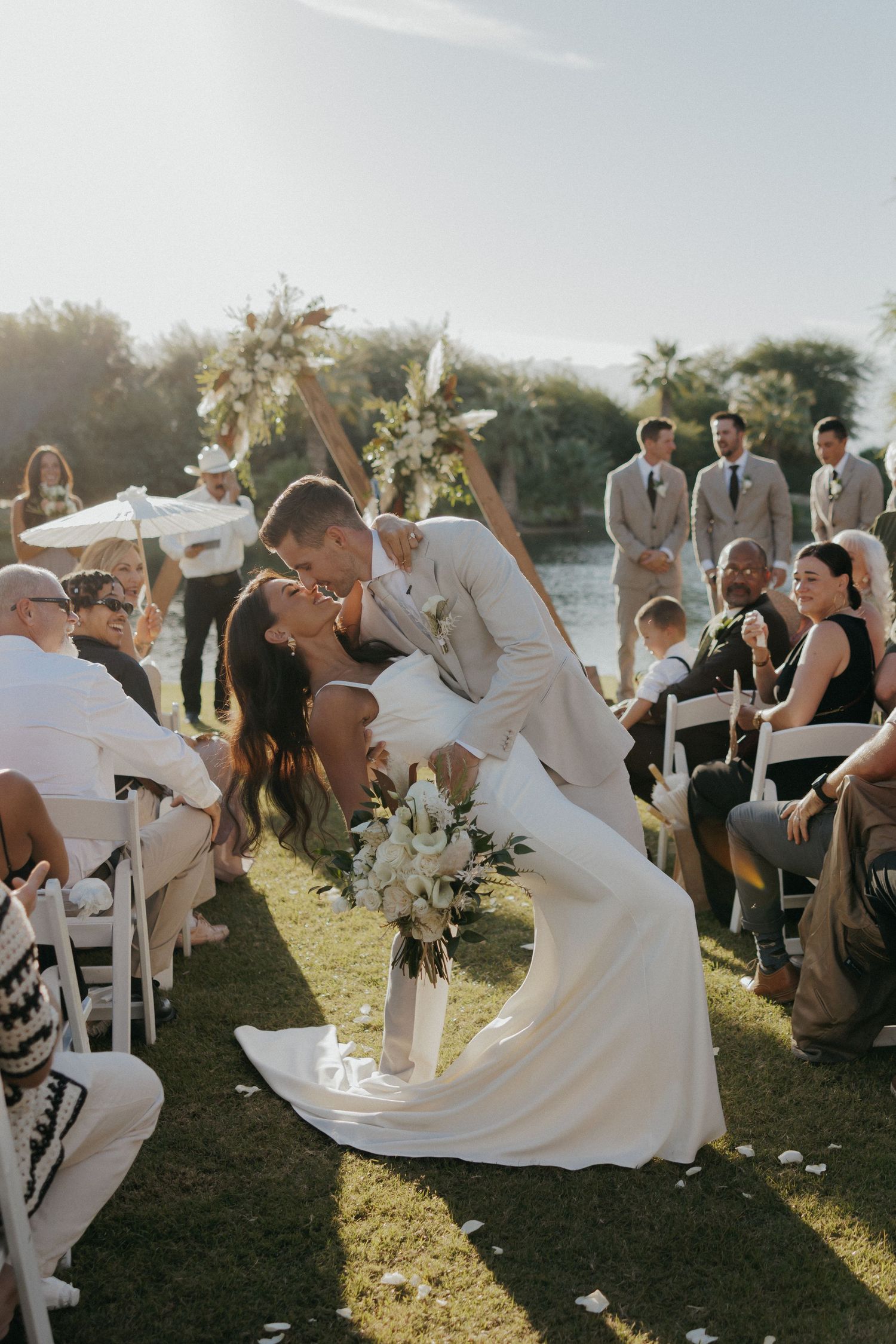 Wedding guests enjoy an outdoor celebration as sunlight glows through a white flowing dress in the breeze.