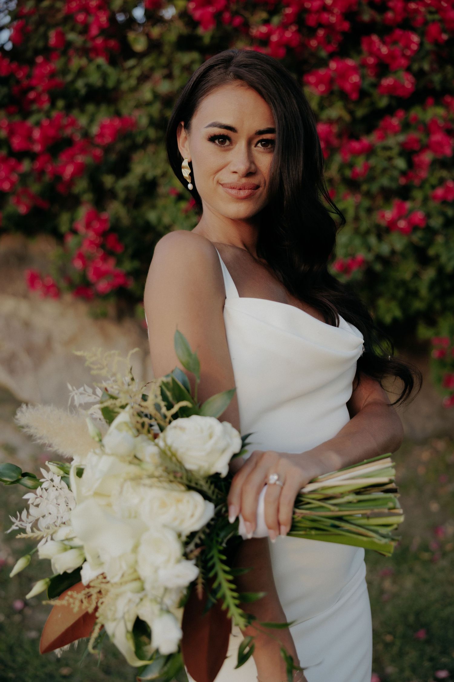 Bridal portrait series with white wedding gown and bouquet against vibrant red floral background in garden setting.