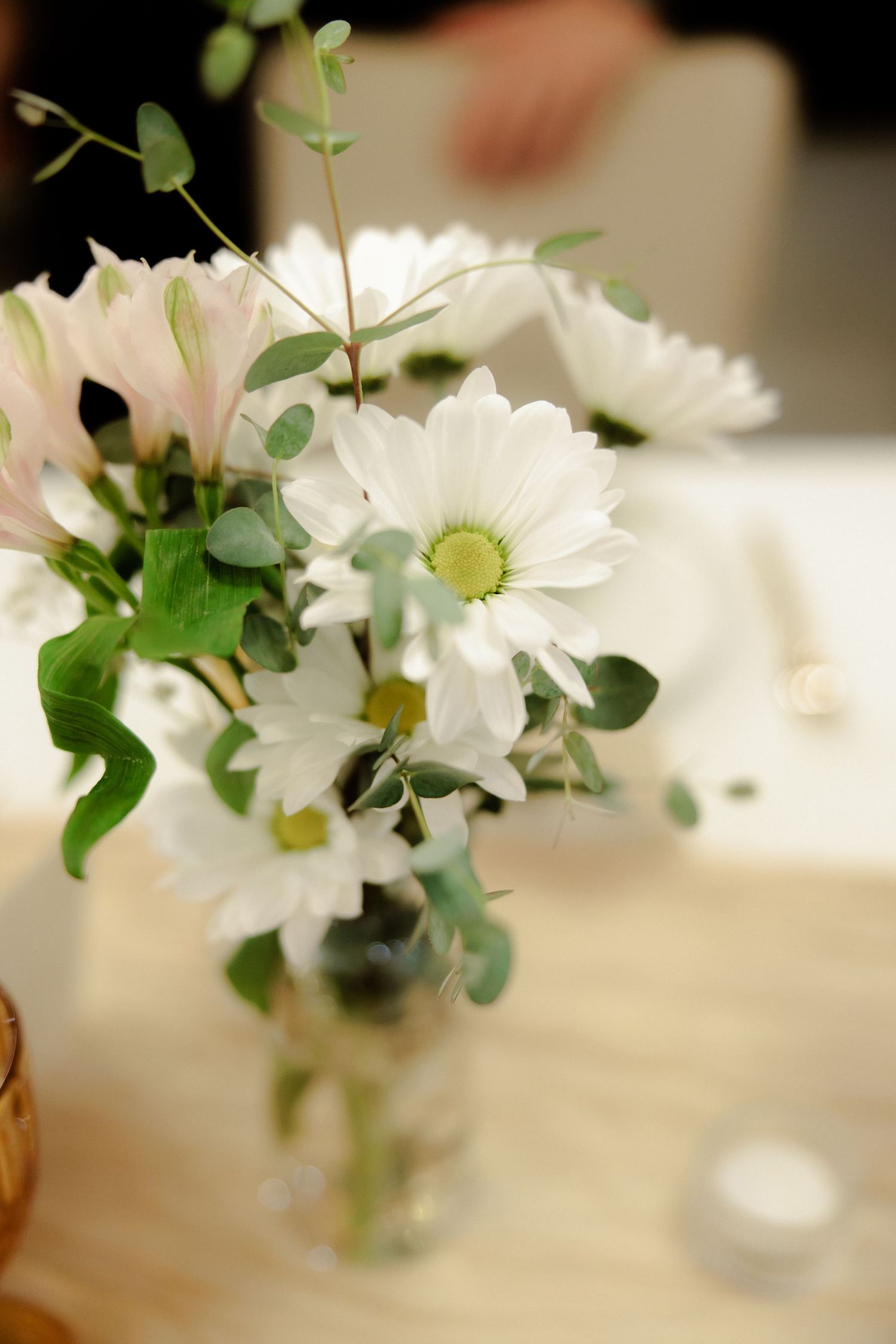 White daisies and eucalyptus leaves arranged in glass vases create an elegant minimalist table centerpiece display.