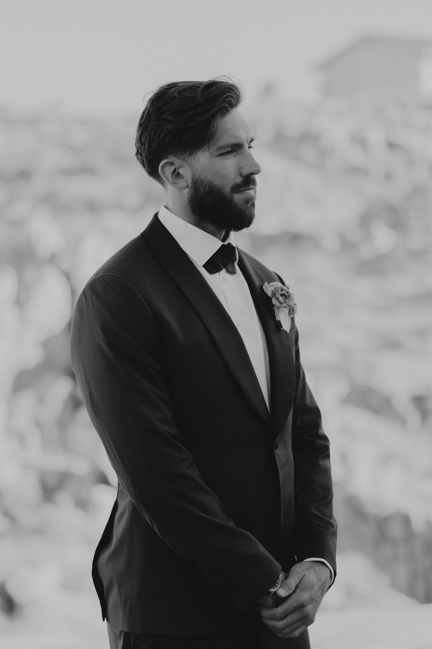 Black and white photos show a groom in a dark suit standing outside against a blurred background.