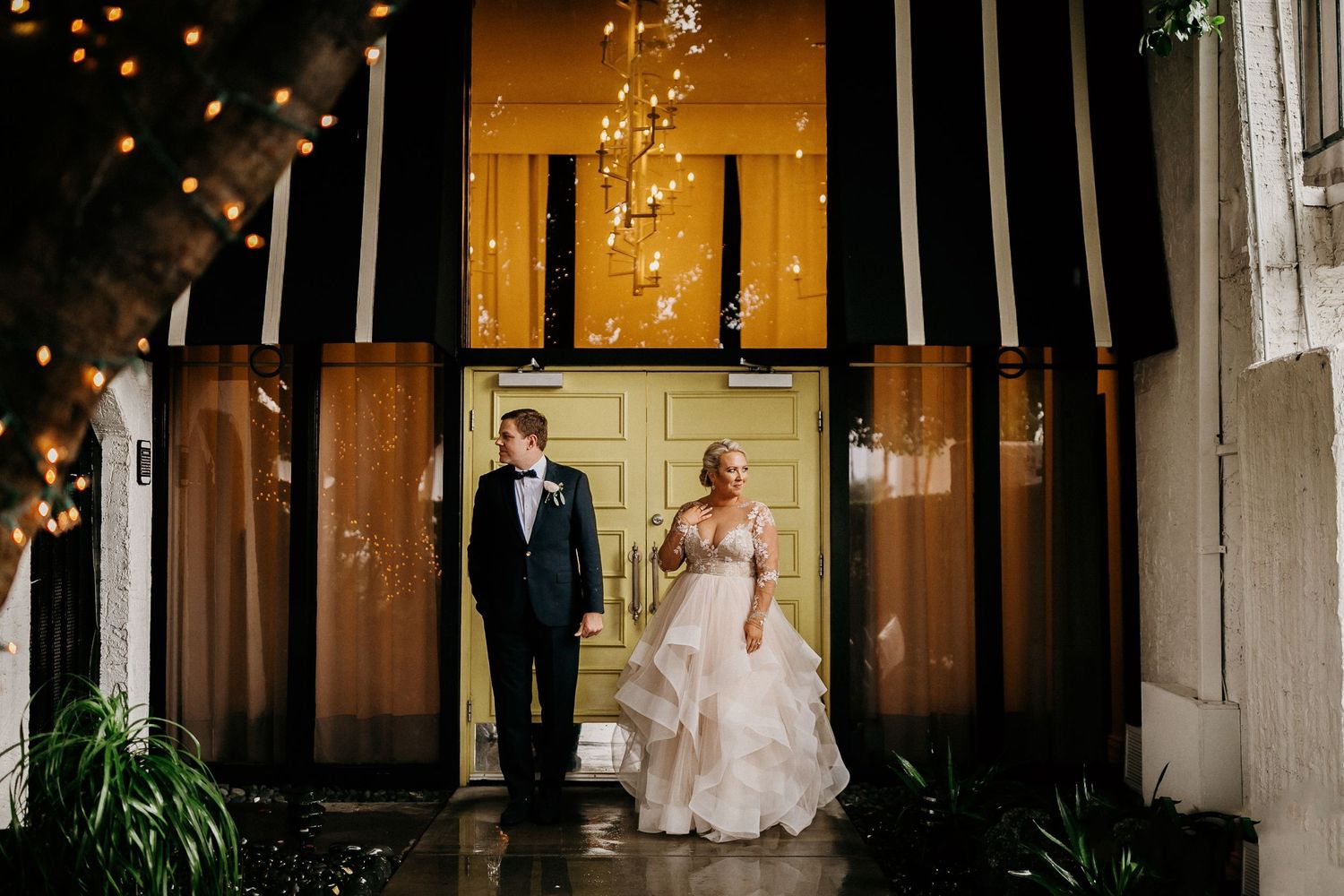 A bride and groom share a romantic dance together in a rustic wooden barn with glowing string lights overhead.