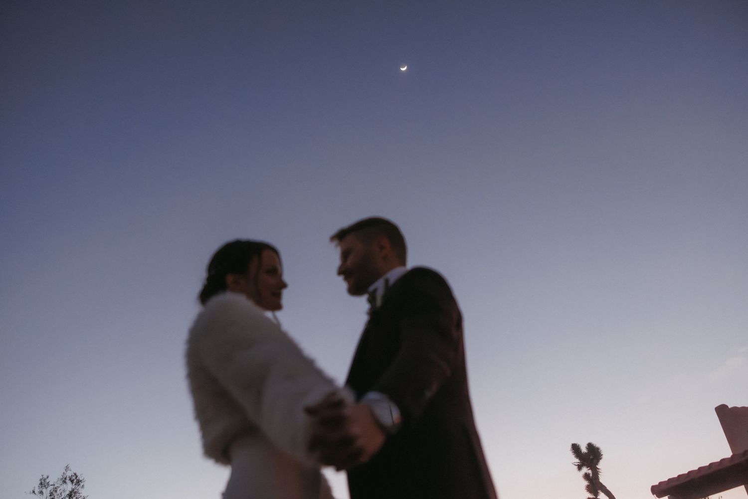 Couple sharing romantic moment at dusk with crescent moon above during outdoor wedding ceremony.