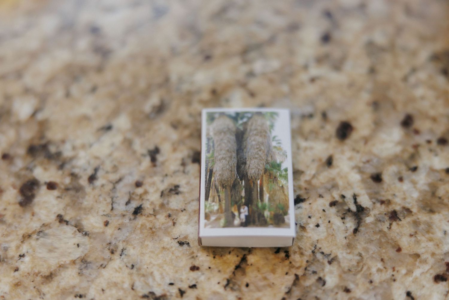 Small rectangular keepsake charm with pressed botanical image on granite countertop wedding detail.