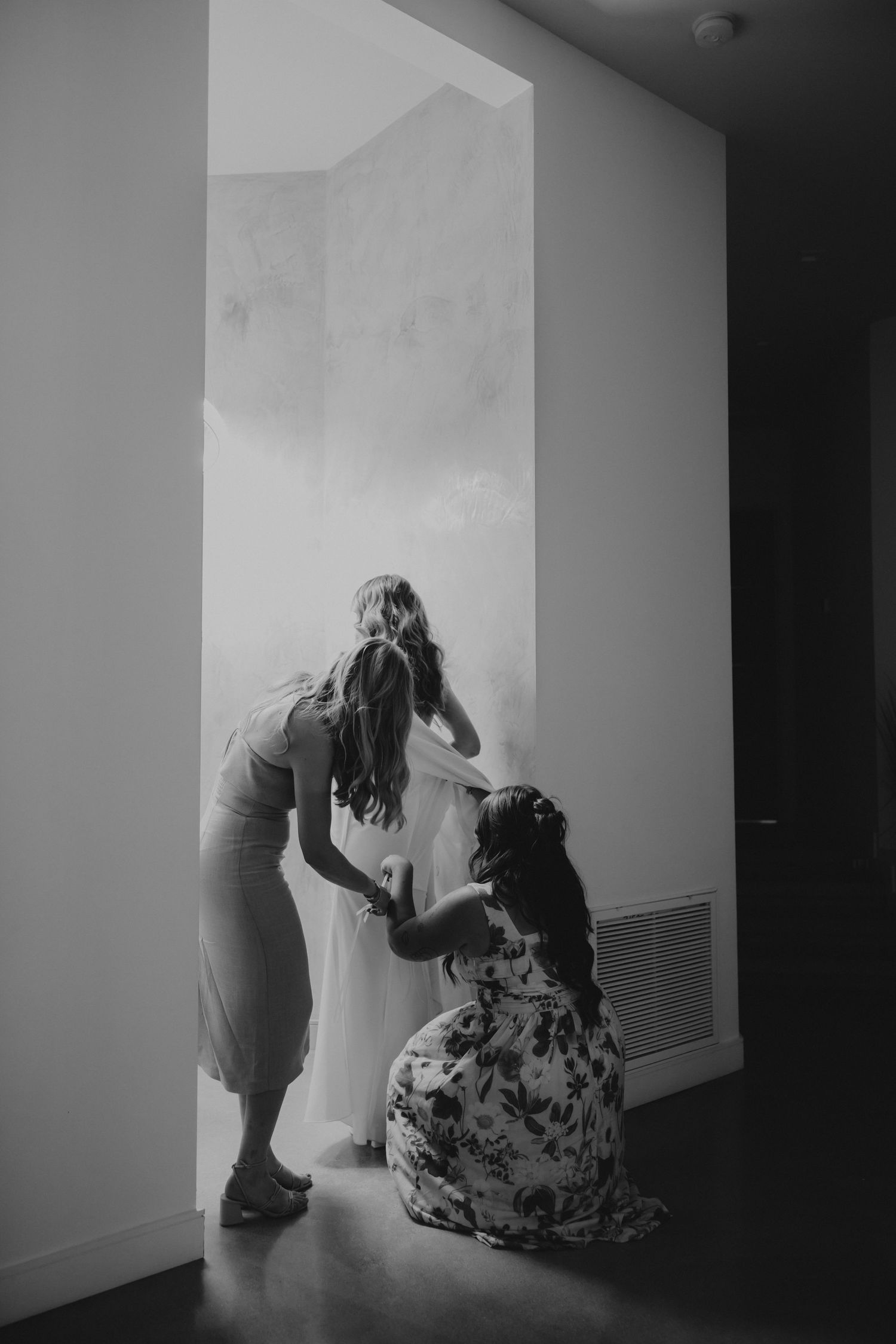 A black and white artistic photo showing two figures in a minimalist white interior space.