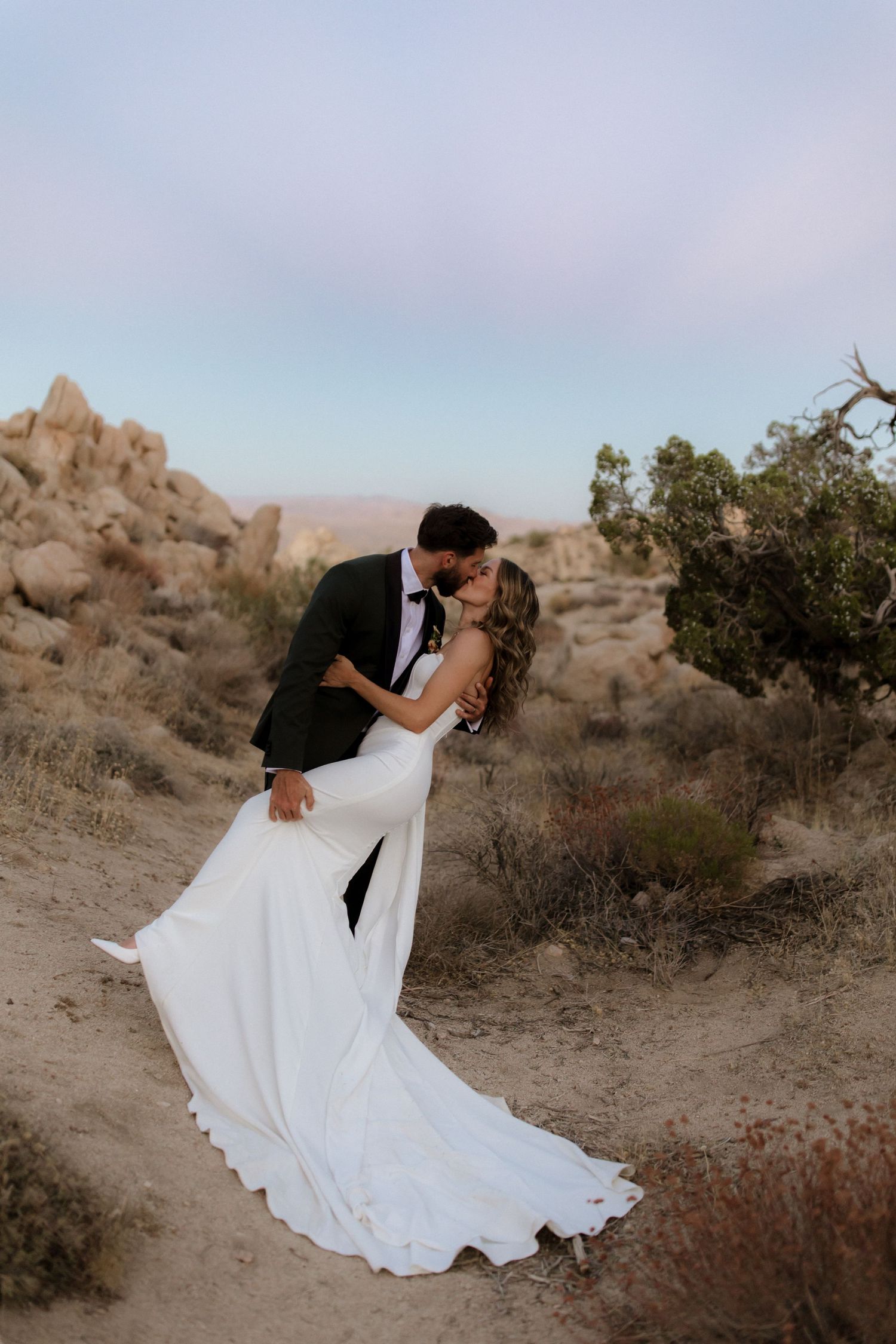 A romantic dance dip photographed in a desert landscape at sunset with desert brush and rock formations in the background.