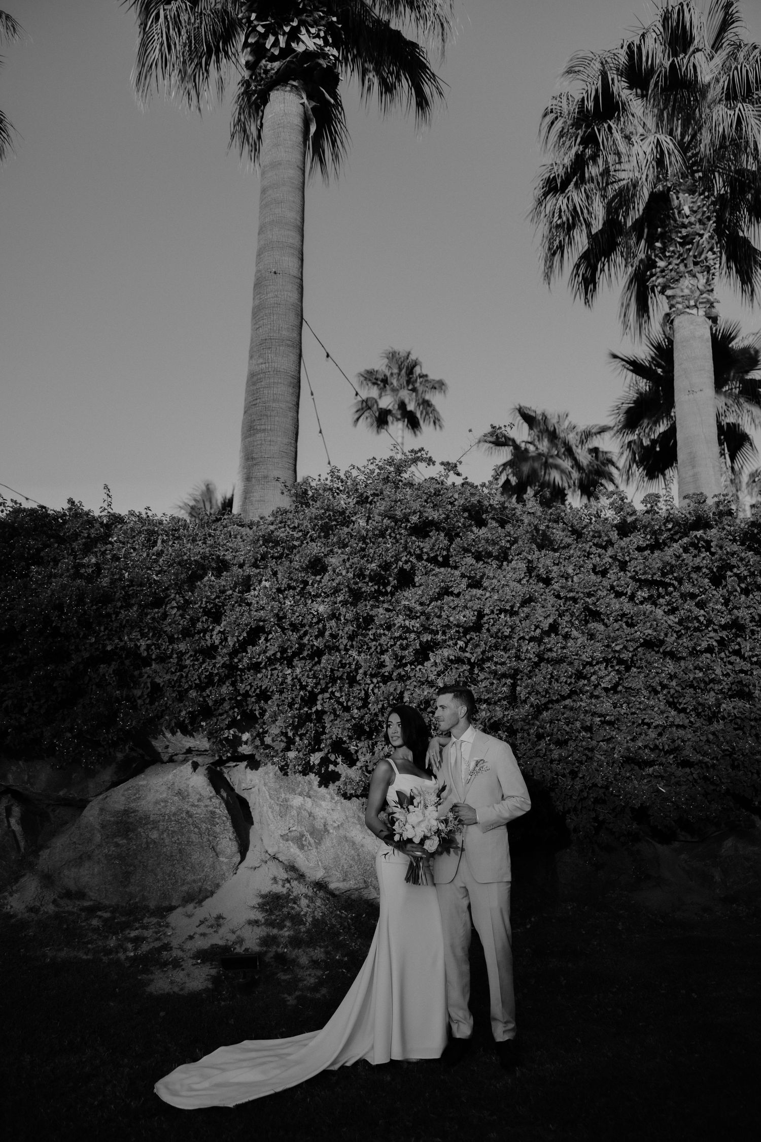 Black and white romantic garden wedding photo with palm trees and lush greenery backdrop at an outdoor venue.