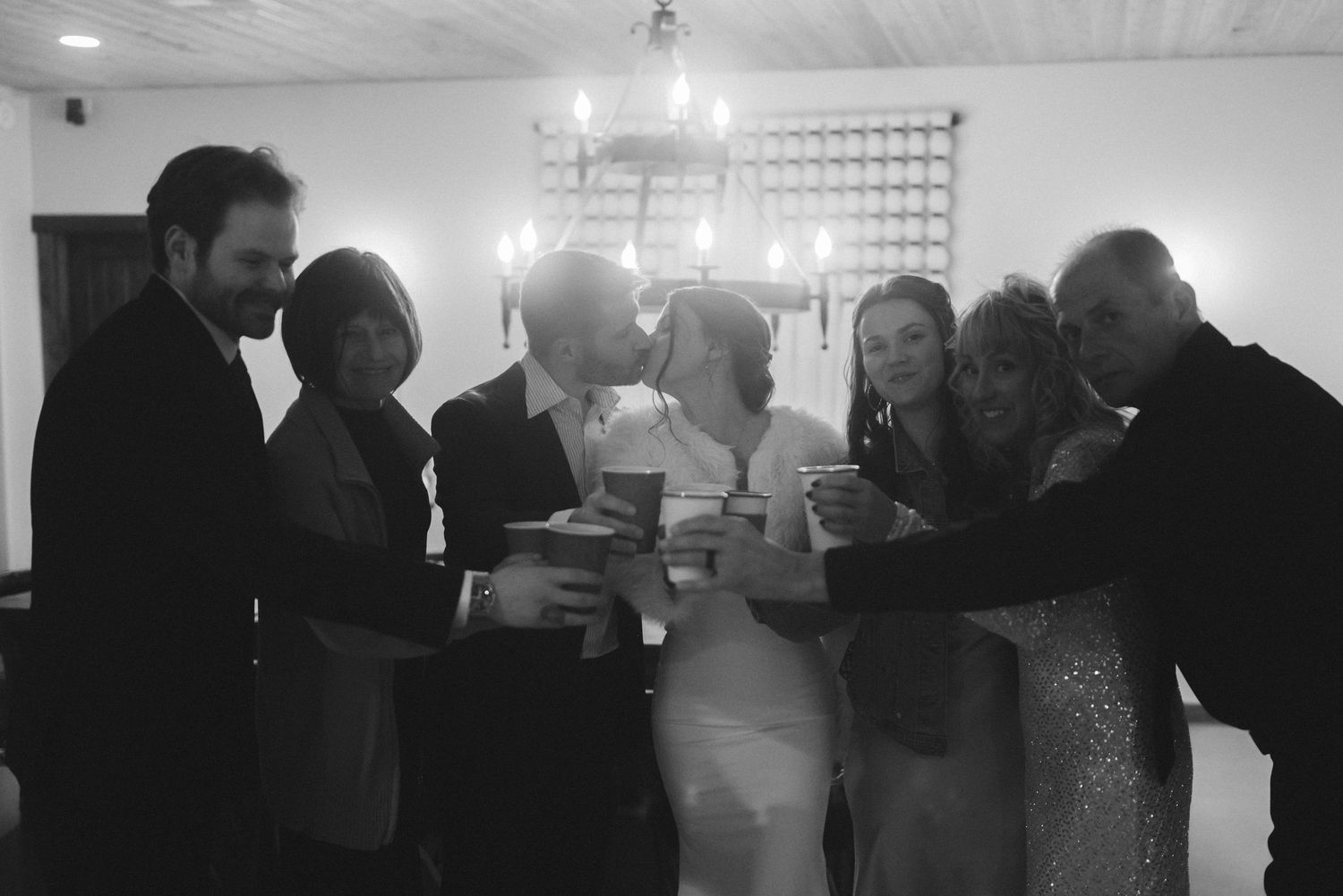 Black and white photo of bride, groom, and family toasting together at indoor reception.