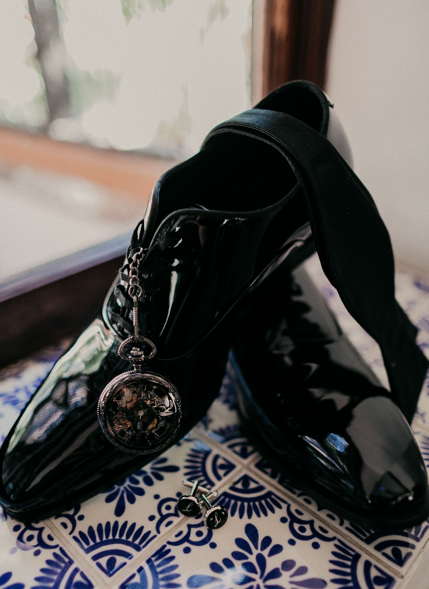 Black lace-up shoes lie on decorative blue and white porcelain-style patterned tiles with floral motifs.