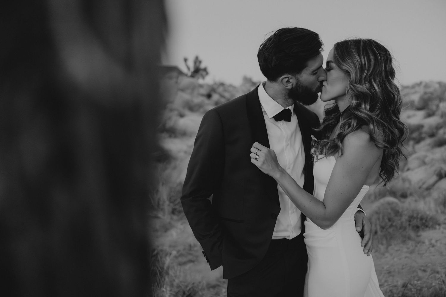 Black and white romantic wedding photoshoot in an outdoor desert setting with dramatic mountain backdrop.
