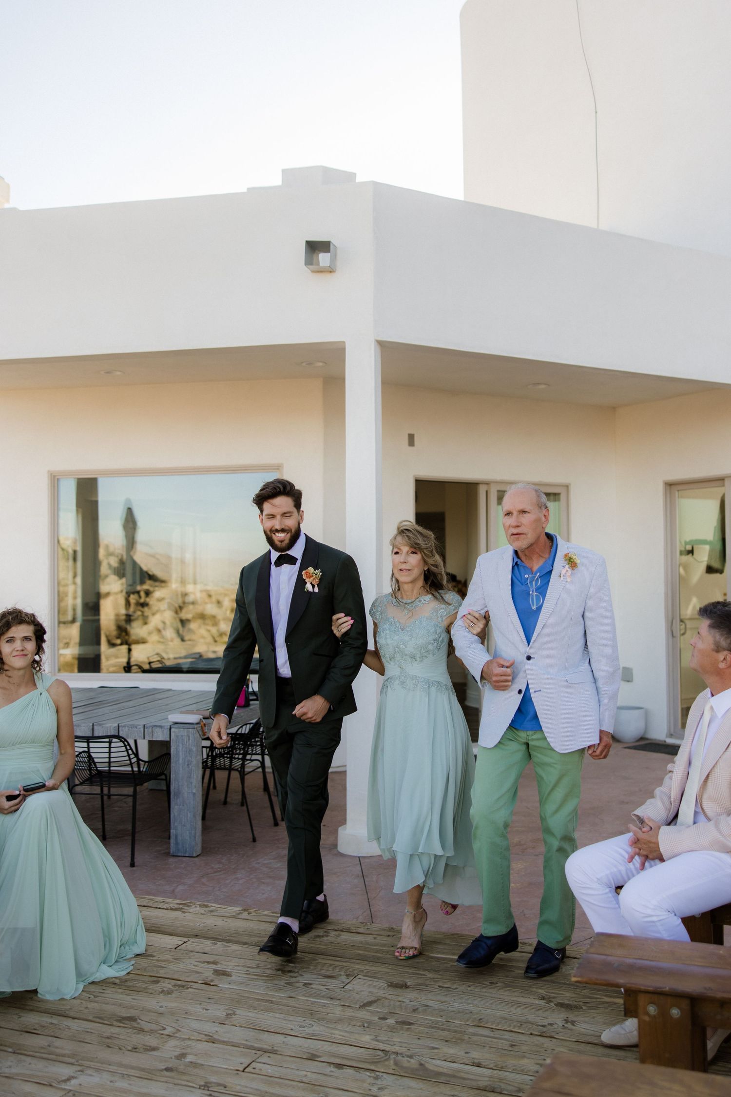 Wedding party poses and interacts on a light-colored patio with mint green bridesmaid dresses and formal attire.