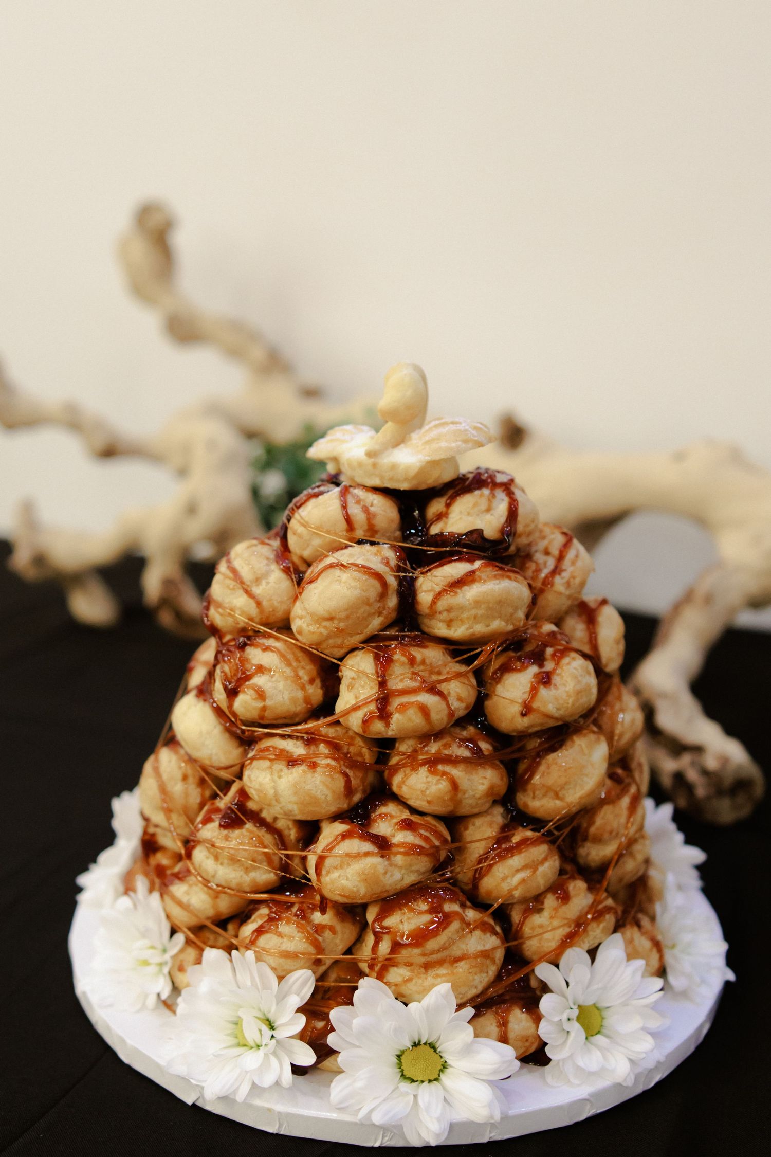 Profiteroles drizzled with caramel sauce arranged on a white plate decorated with small white daisies.