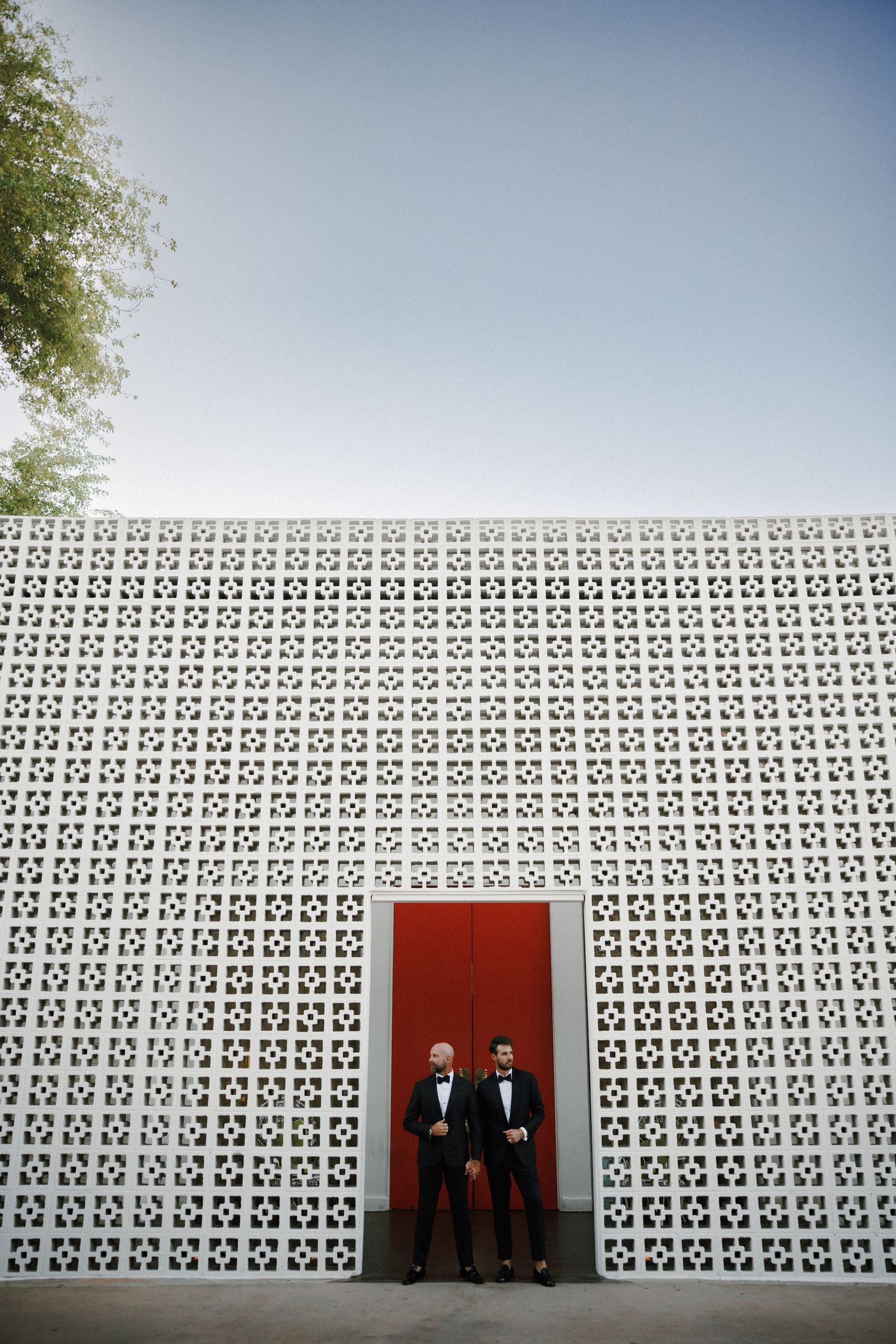 A black and white photo of two figures standing in front of a geometric patterned wall with a red doorway.