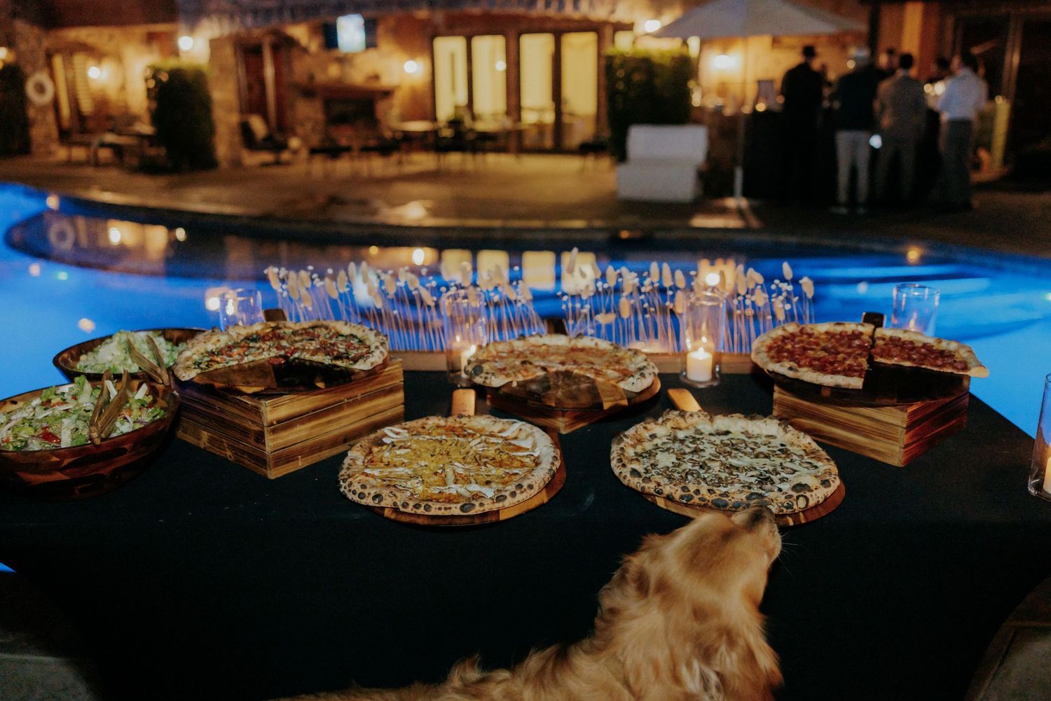 An elegant evening event setup features a pool, illuminated dining tables, and stylish decorative elements at dusk.