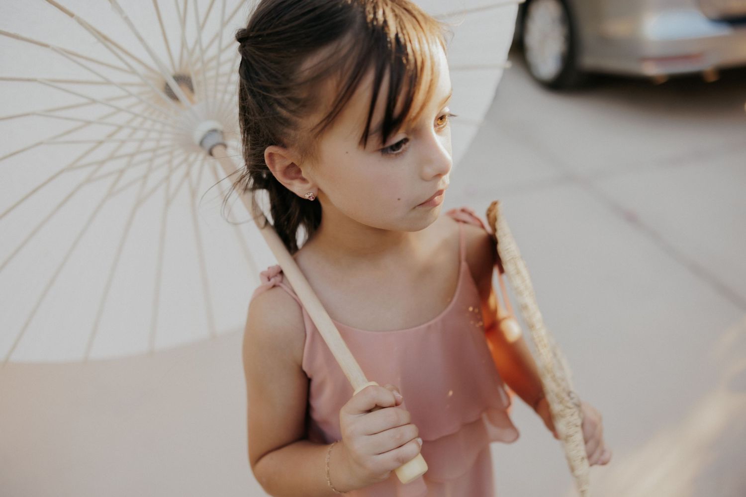 A little girl in a pink dress plays with white parasols during a dreamy indoor photoshoot.