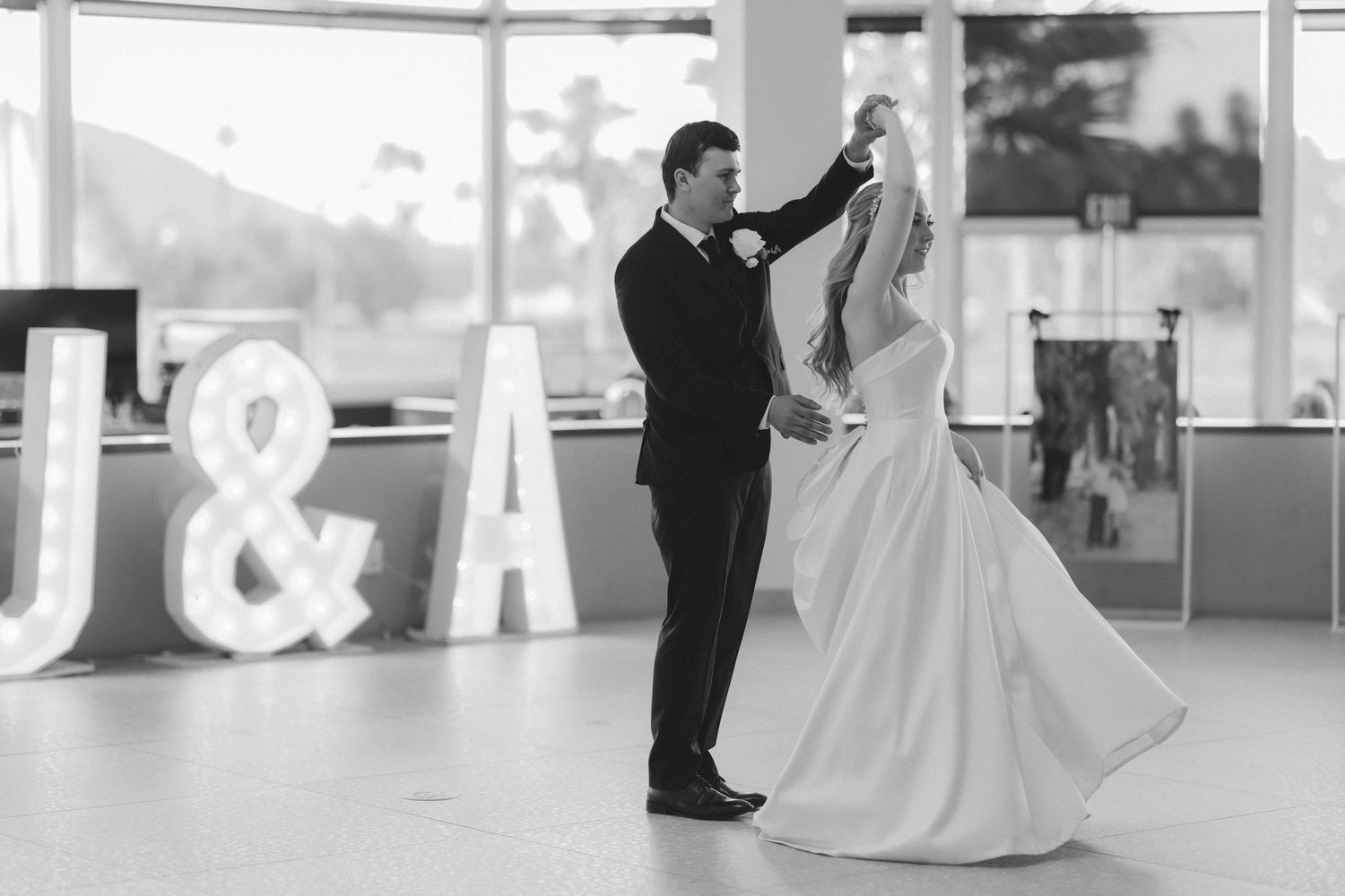 Bride and groom sharing first dance in front of illuminated J&A marquee letters at wedding reception.