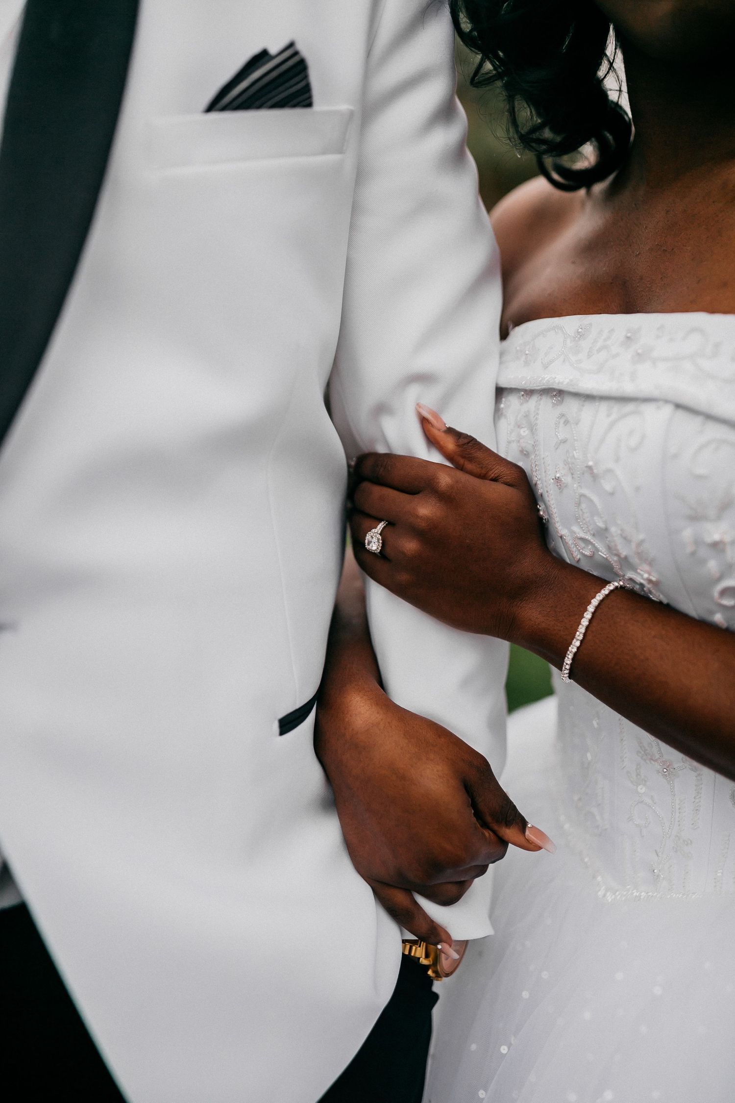 Cropped side view of newlyweds embracing with focus on white wedding dress and suit details.