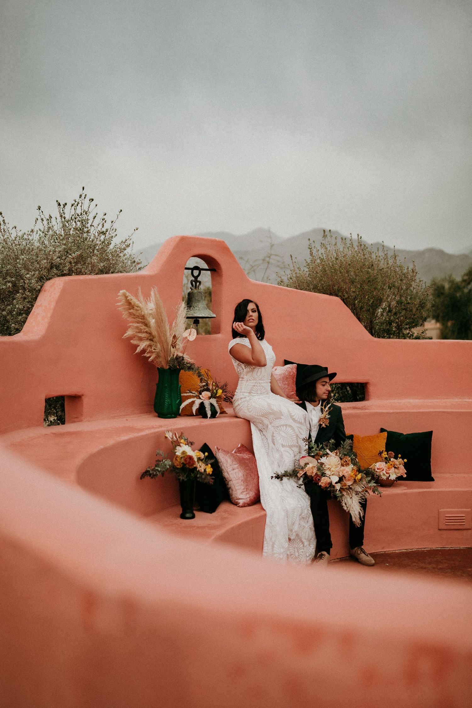 Wedding couple posing against terra cotta colored adobe wall in desert landscape.