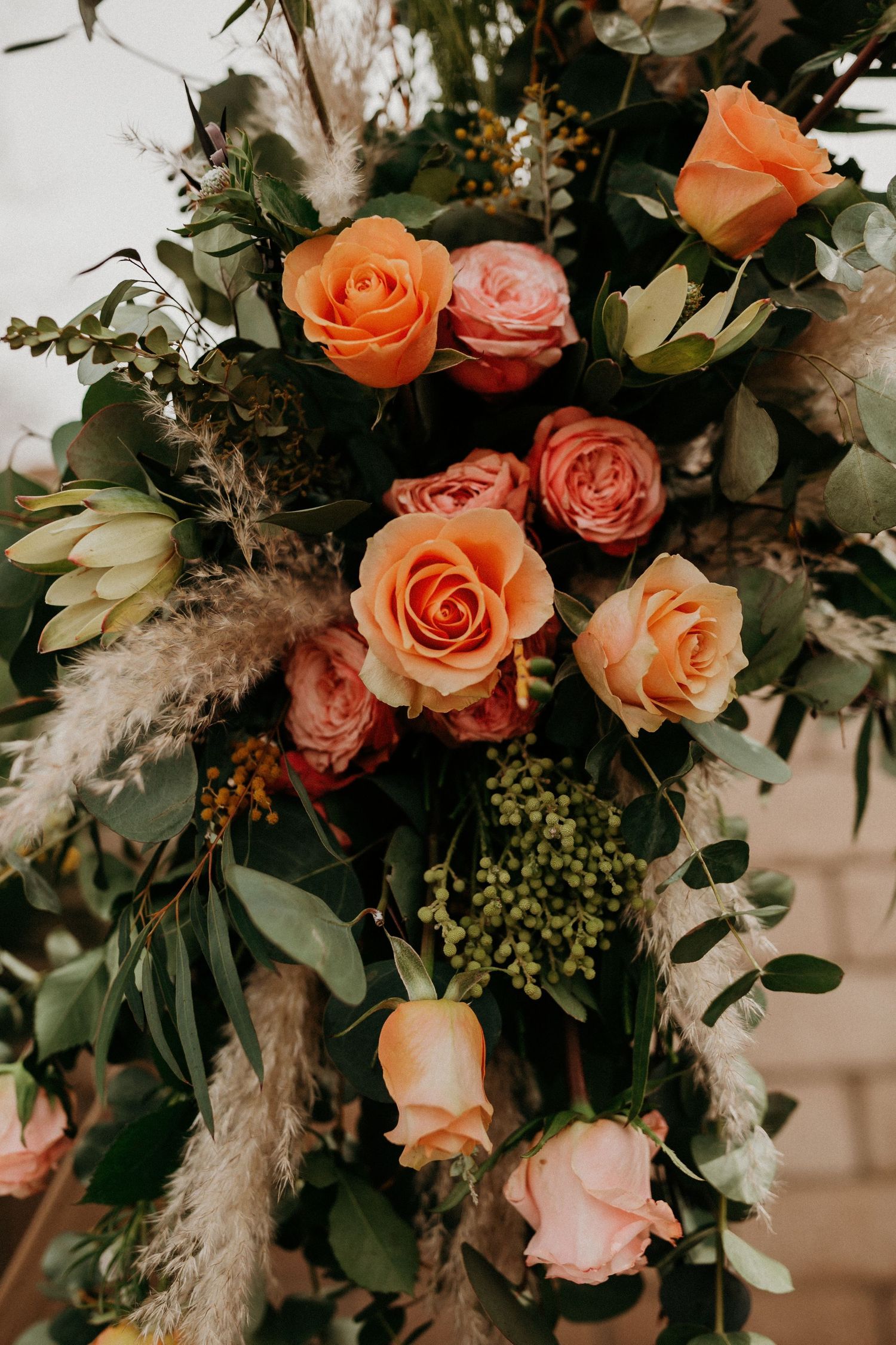 Close-up of luxurious floral arrangement featuring peach roses and eucalyptus with pampas grass accents.