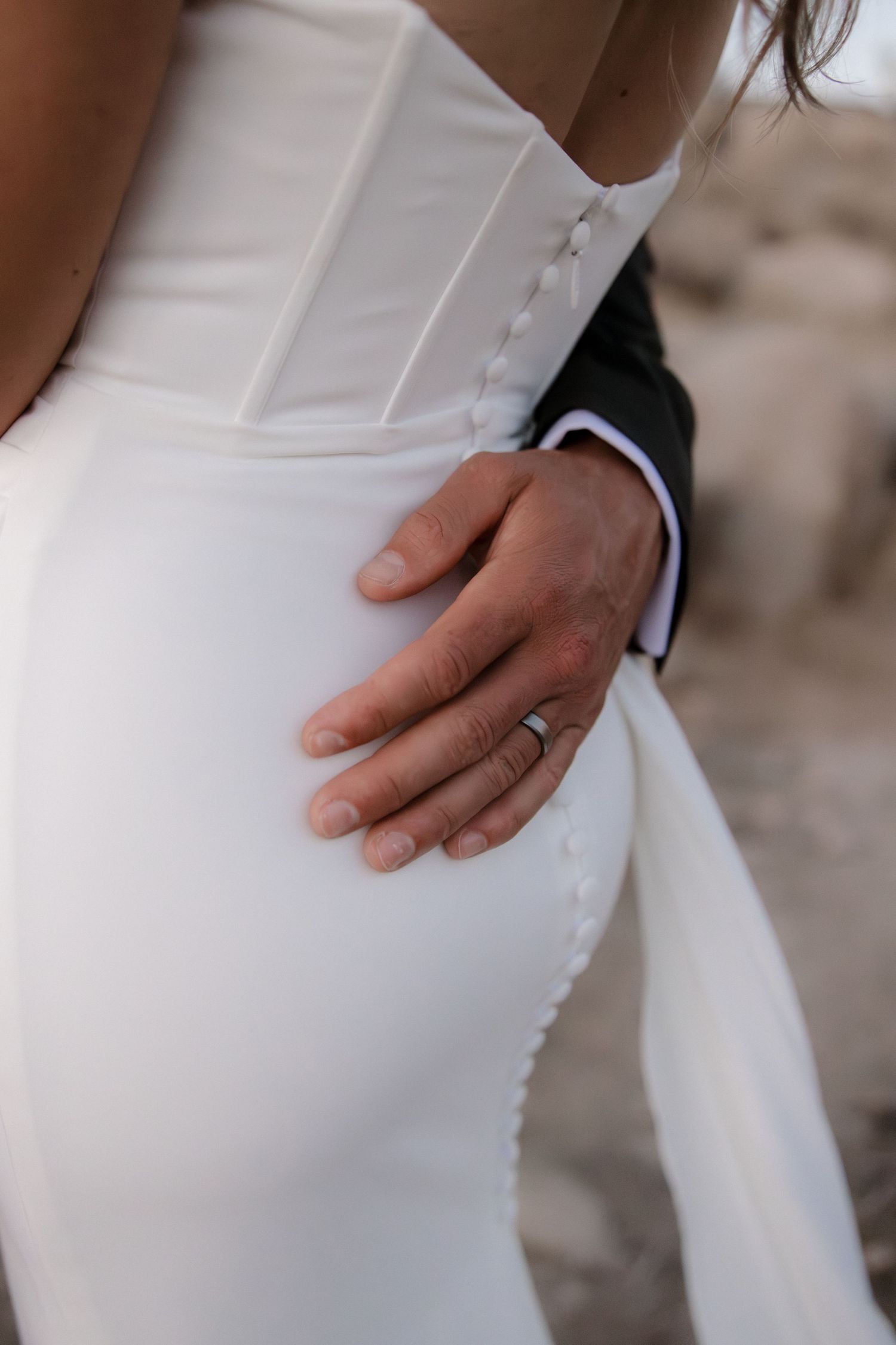 Close-up detail shots of hands resting on a white wedding dress showing delicate fabric texture and elegant folds.