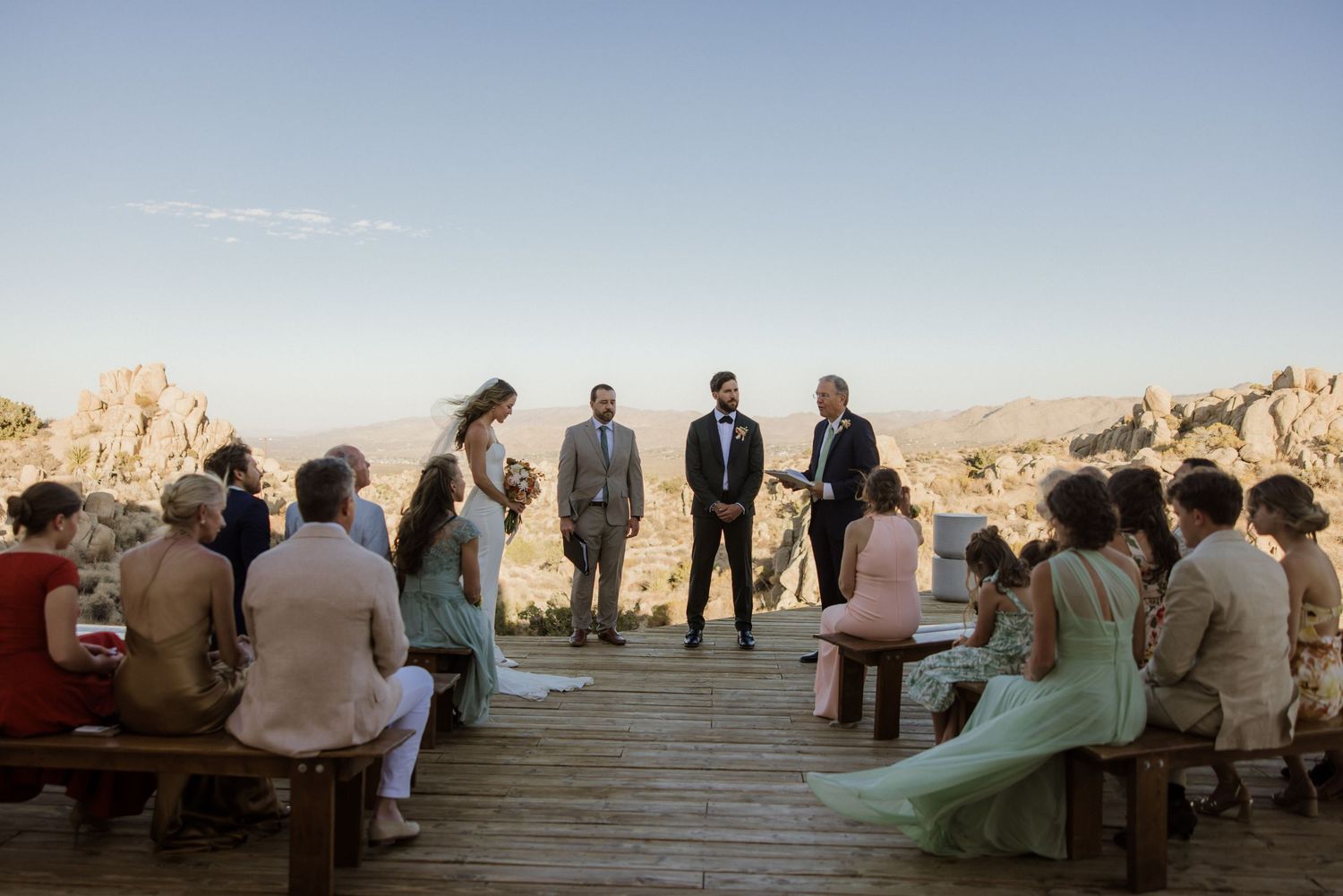 Desert wedding guests seated on wooden benches overlooking majestic canyon landscapes.