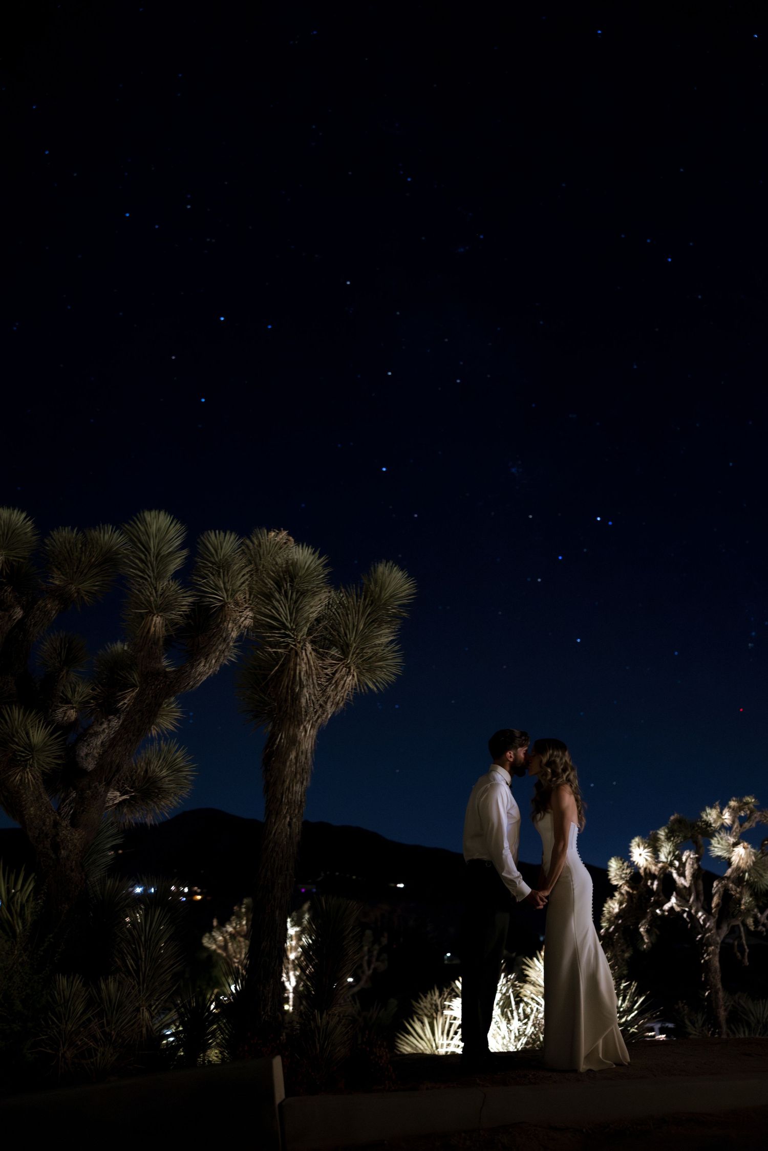 A nighttime desert wedding ceremony beneath starlit skies and illuminated Joshua trees creates a magical atmosphere.