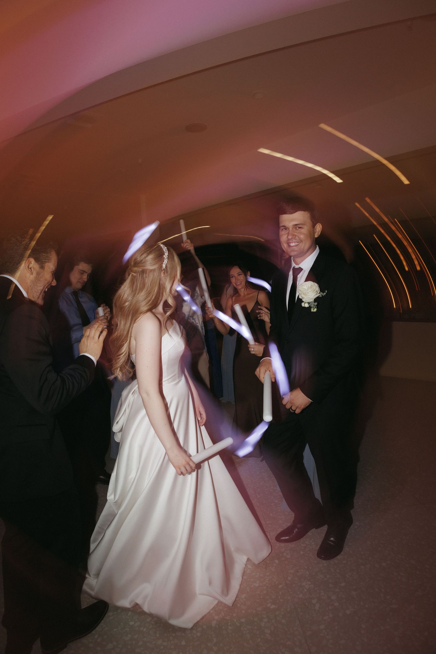 Bride and groom walking through glowing light tunnel at evening wedding reception.