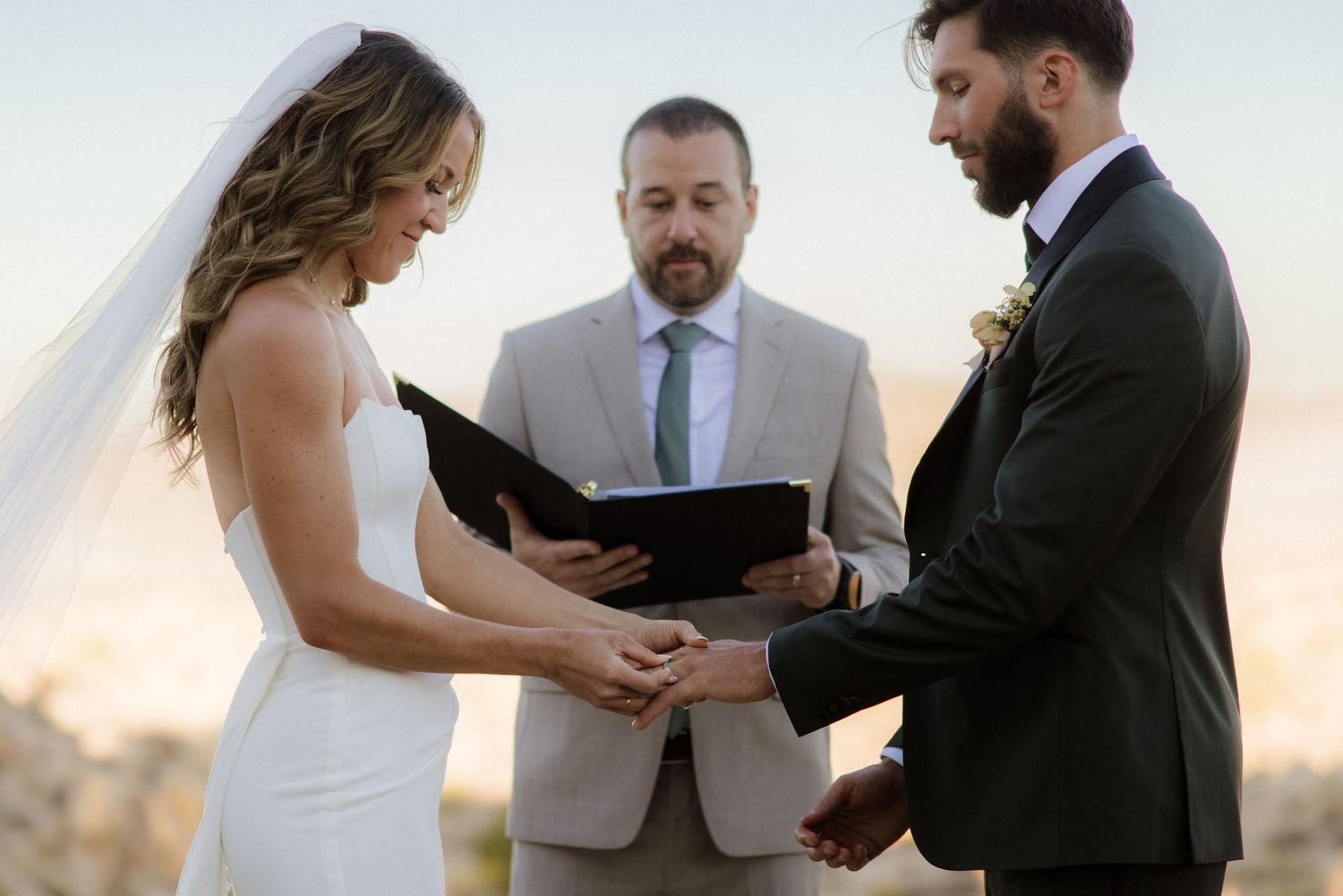 An intimate outdoor wedding ceremony takes place at sunset as a couple holds hands in front of an officiant.