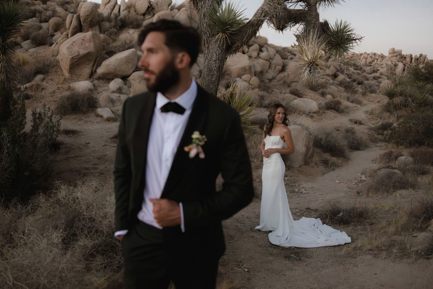 A couple poses for wedding photos in a rugged desert landscape in Joshua Tree National Park at golden hour.