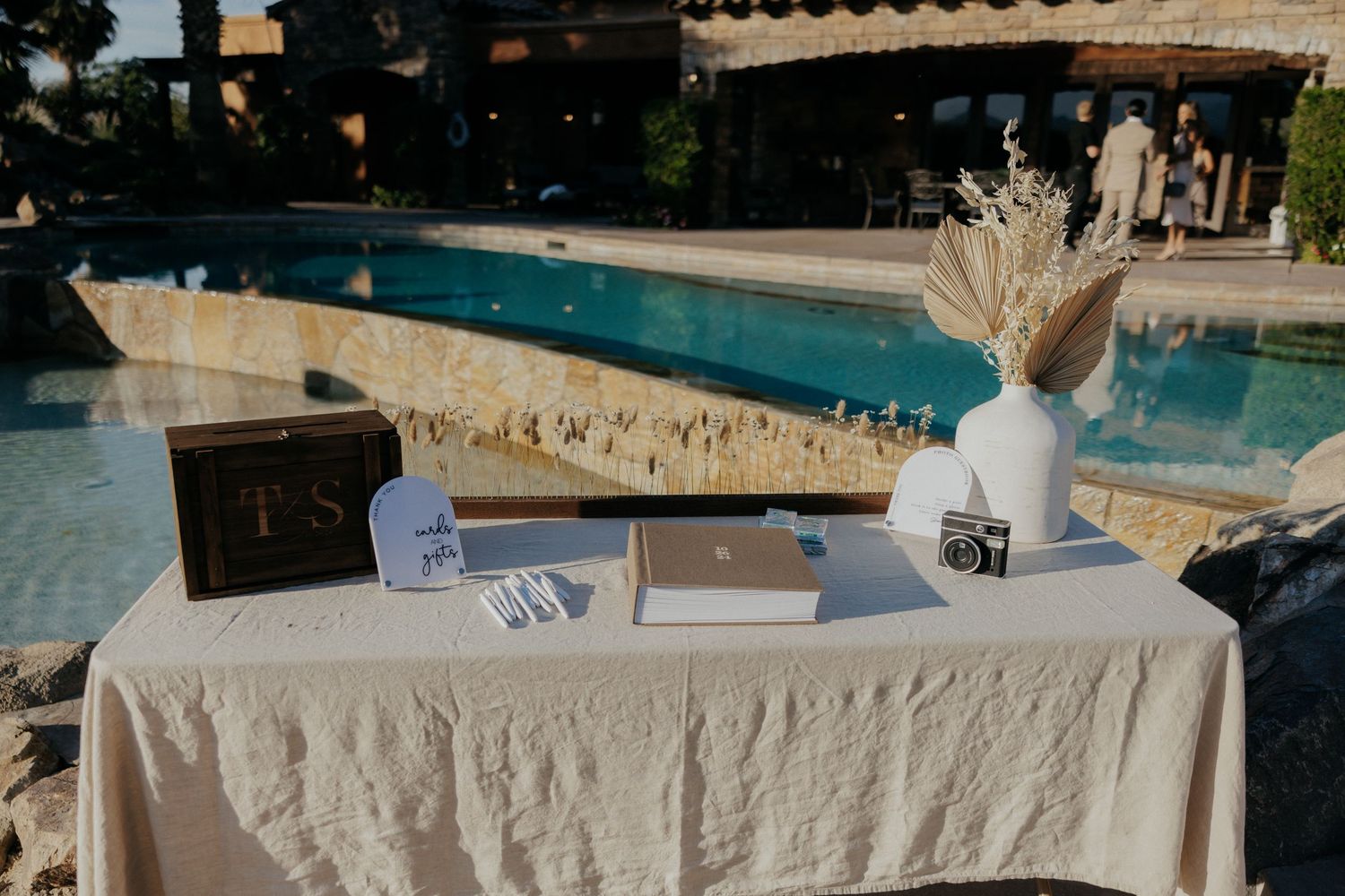 Elegantly decorated outdoor wedding reception tables with white linens and floral centerpieces beside a swimming pool.