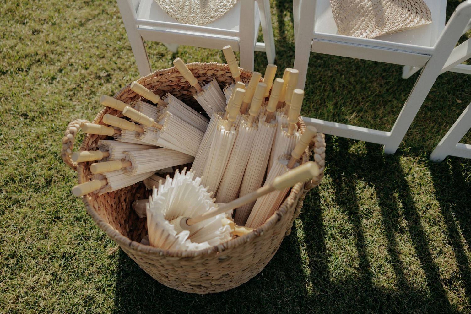 Vintage wooden basket filled with rustic decor elements and white feathers sits on grass in natural sunlight.