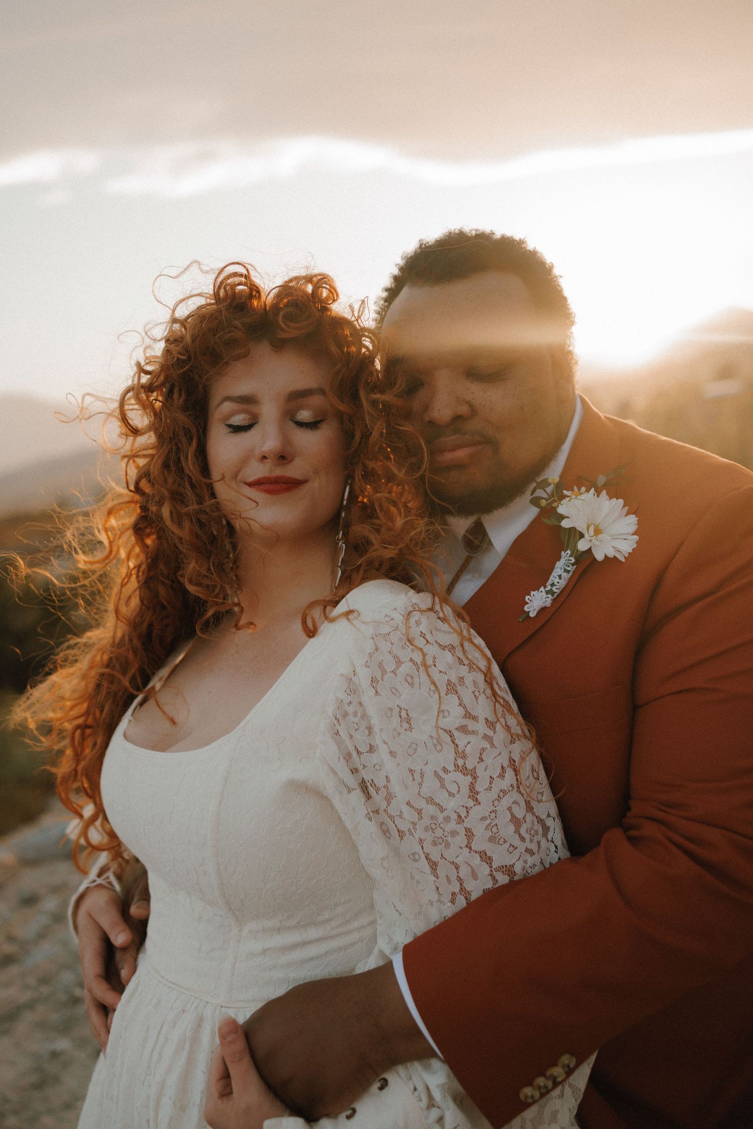 Romantic wedding couple poses together in sunlit field during golden hour portraits.
